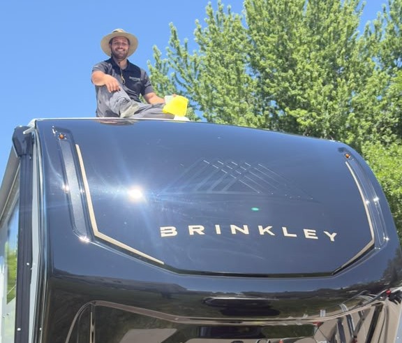 Nomada hand washing a black Brinkley fifth wheel RV at a customer's home in Northern Utah