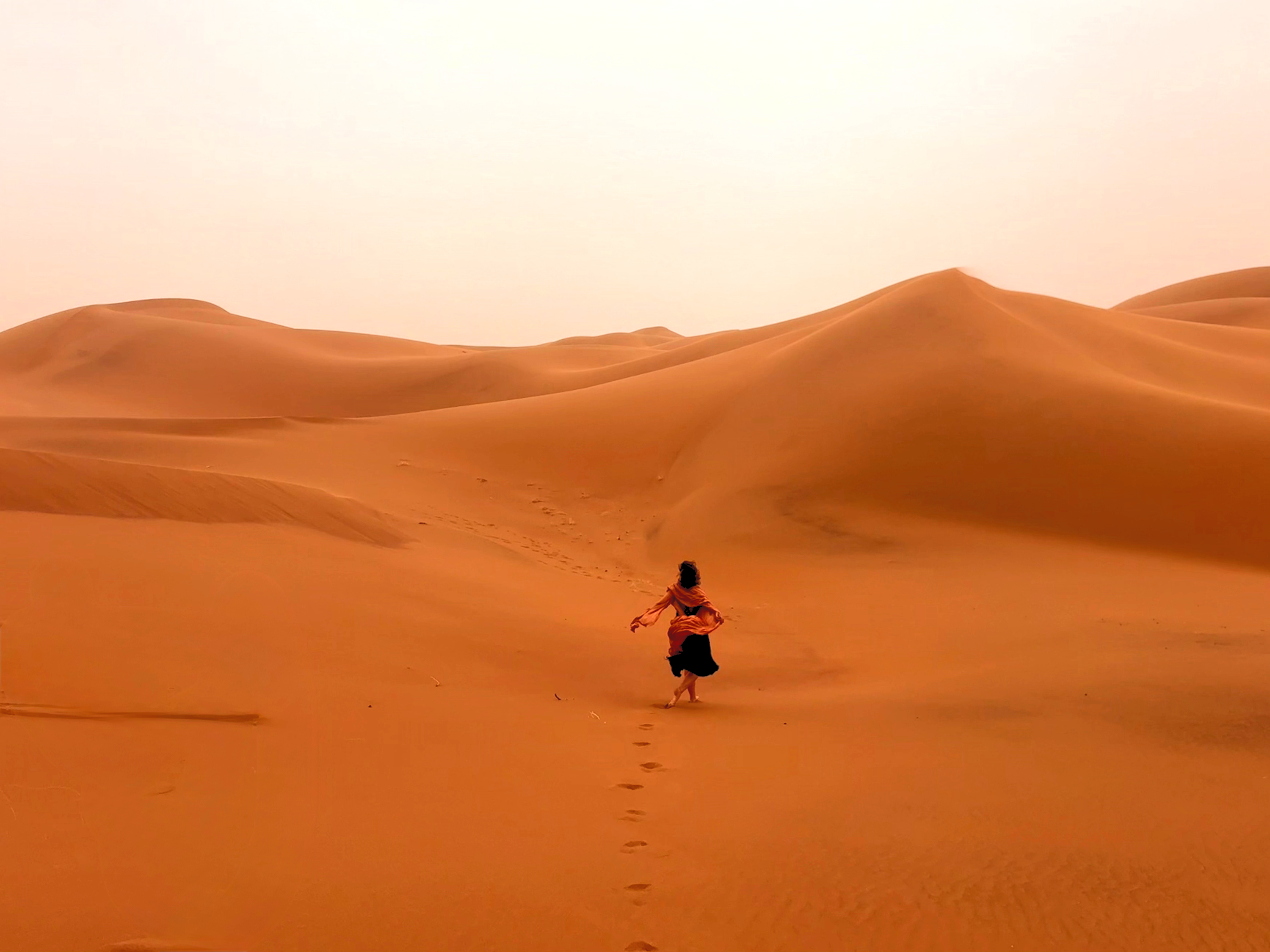 Woman walking across the golden dunes of the Moroccan Sahara