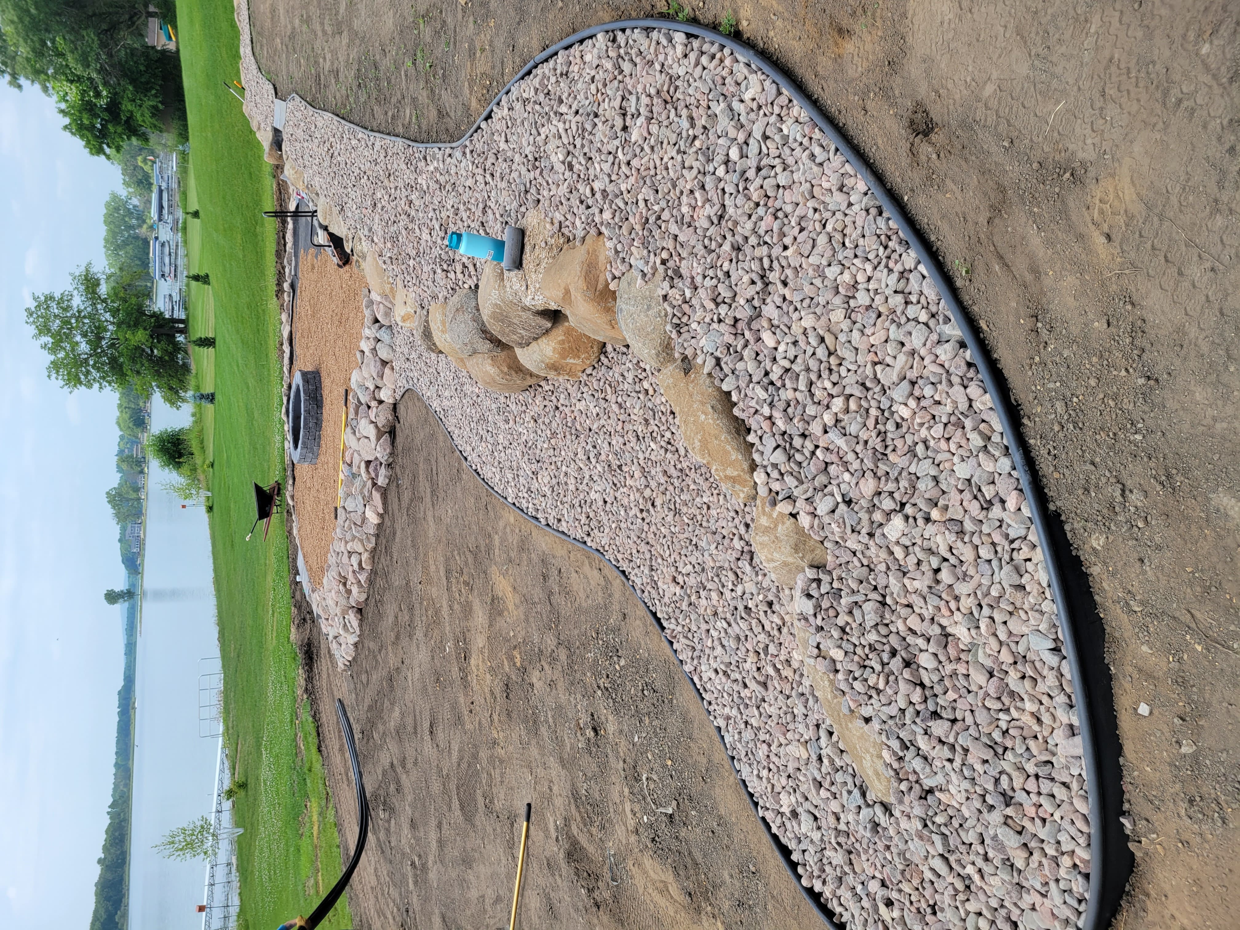 Decorative river rock bed, boulder border, and fire pit landscaping near lake in Dane County, WI