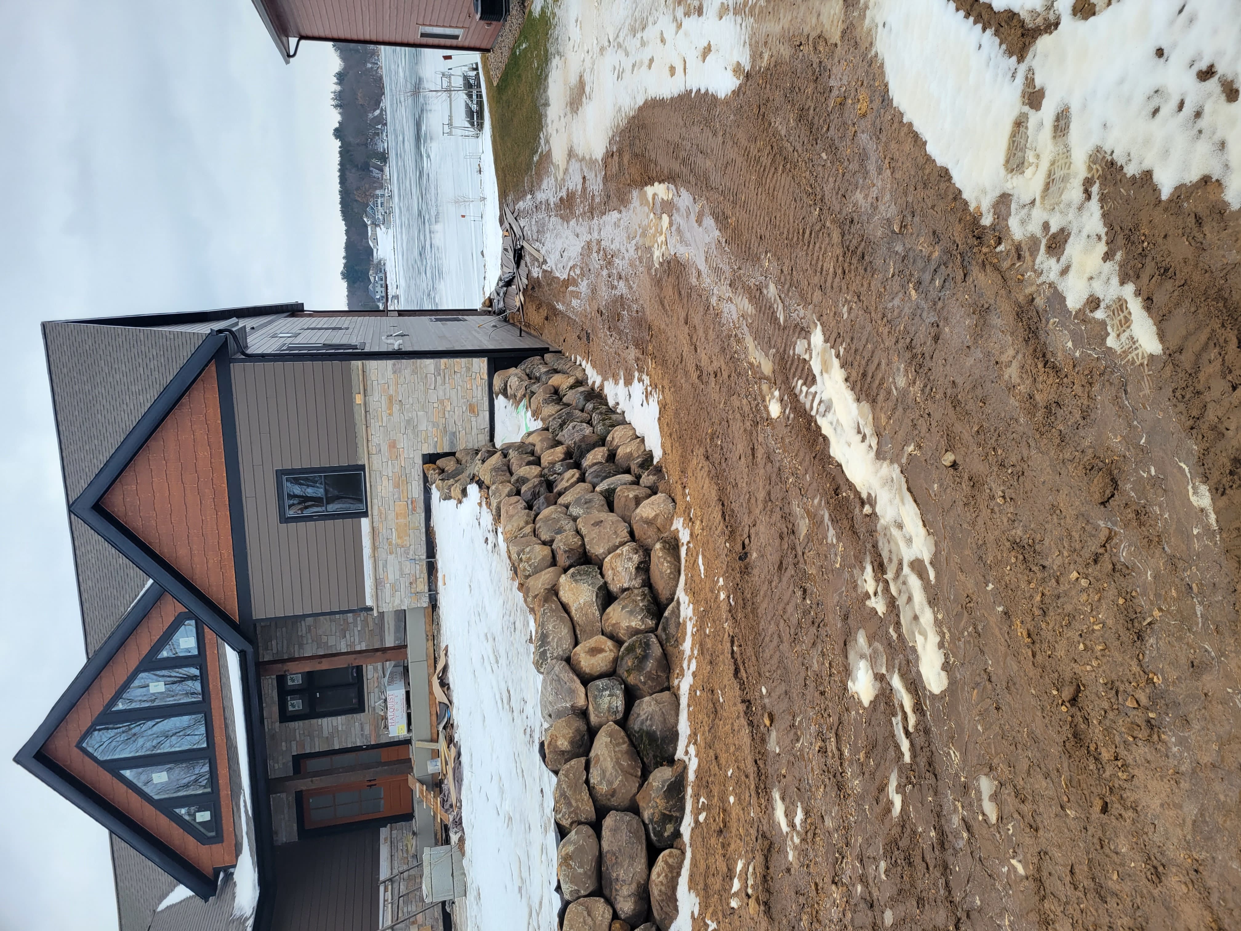 Boulder retaining wall installation along side foundation of custom lake home in Dane County, WI