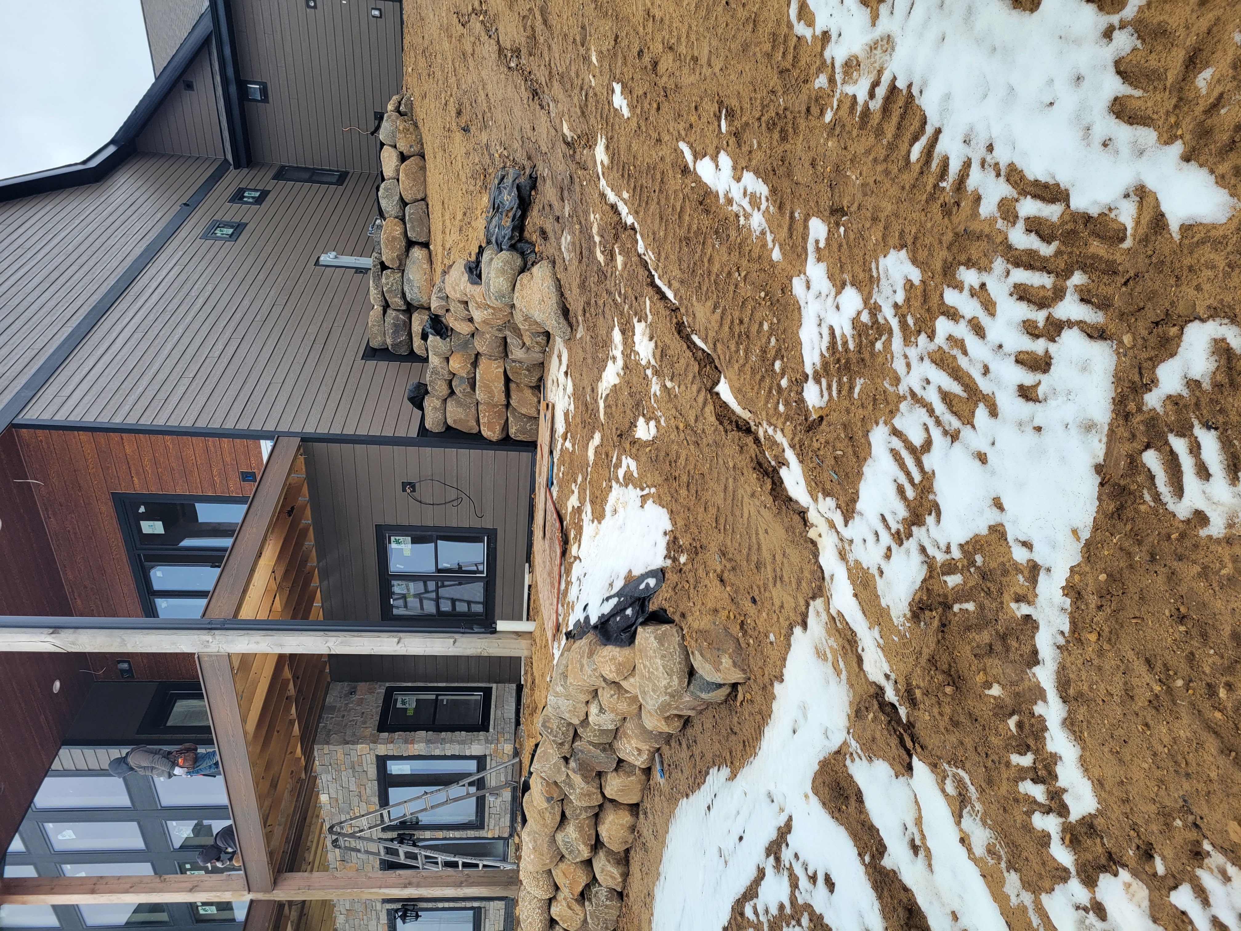 Boulder retaining wall construction along sloped home foundation in Dane County, WI