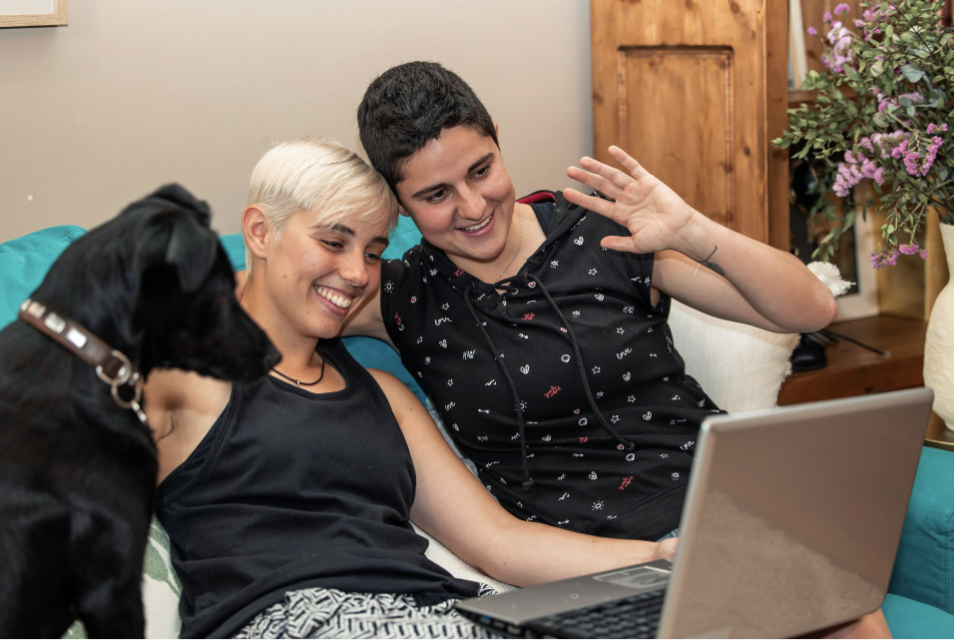 Two people smiling with a black dog during a video call