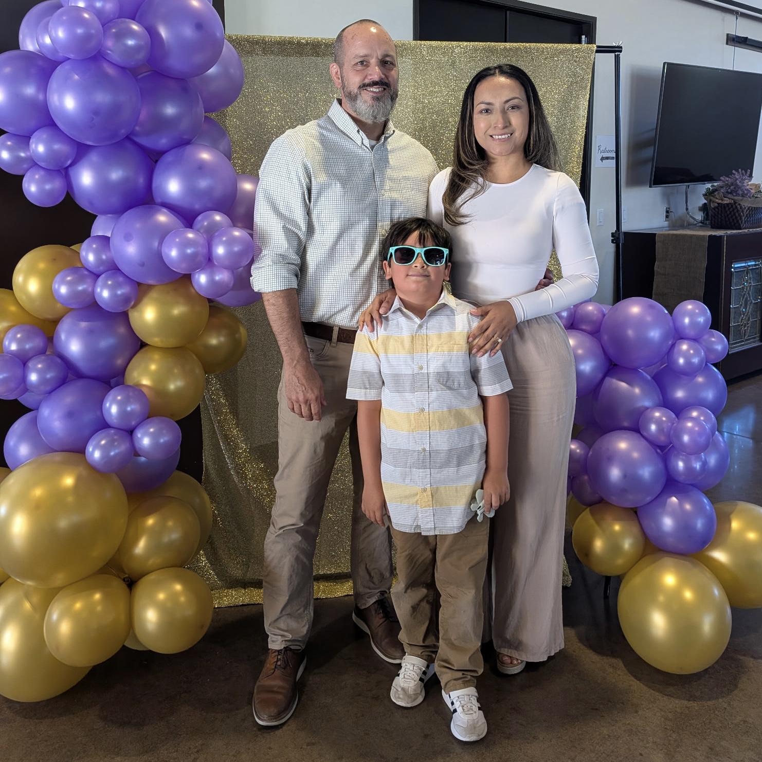 Military family celebrating together in front of a purple and gold balloon arch