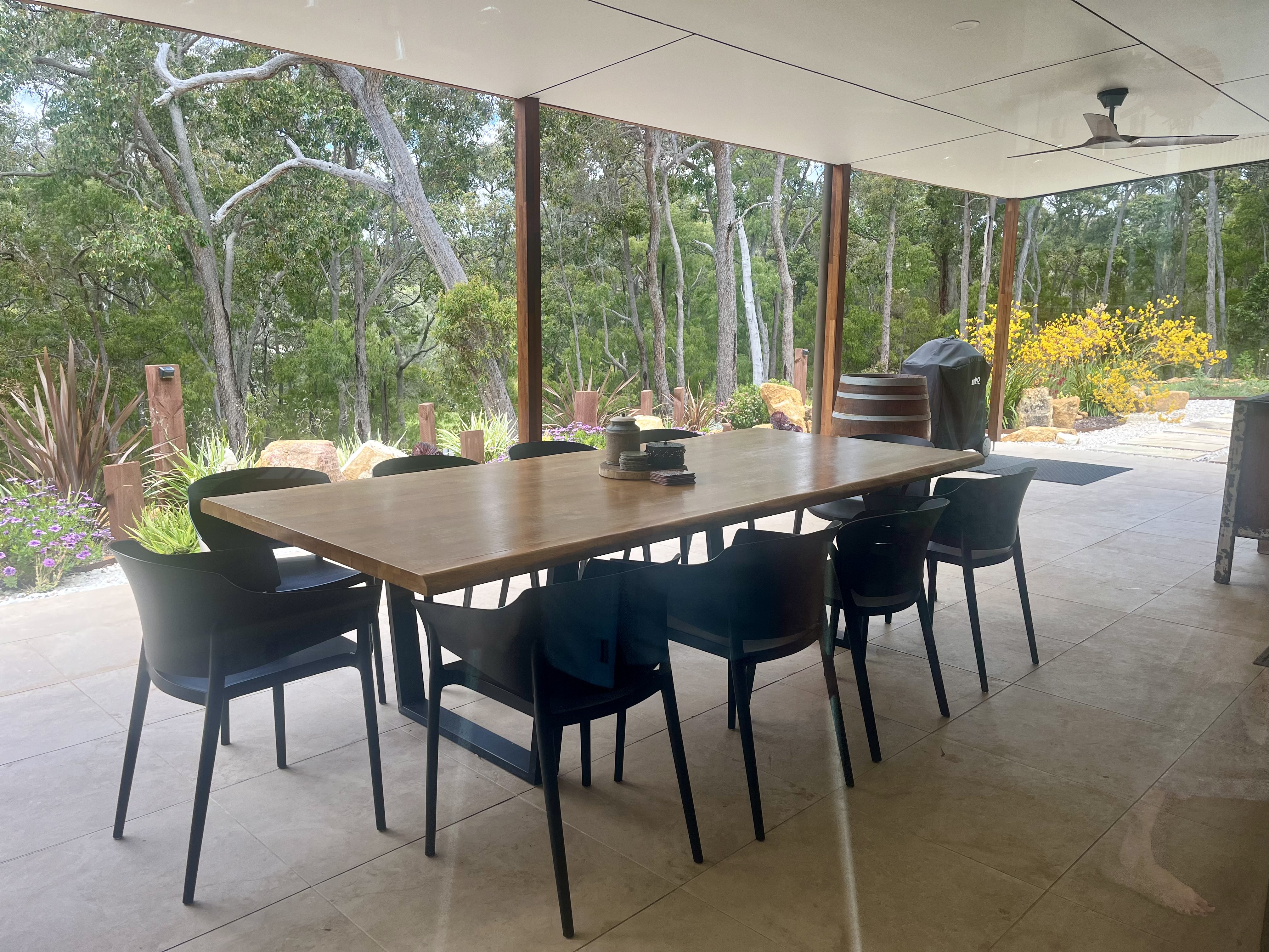 Covered alfresco dining area with long timber table set among bushland
