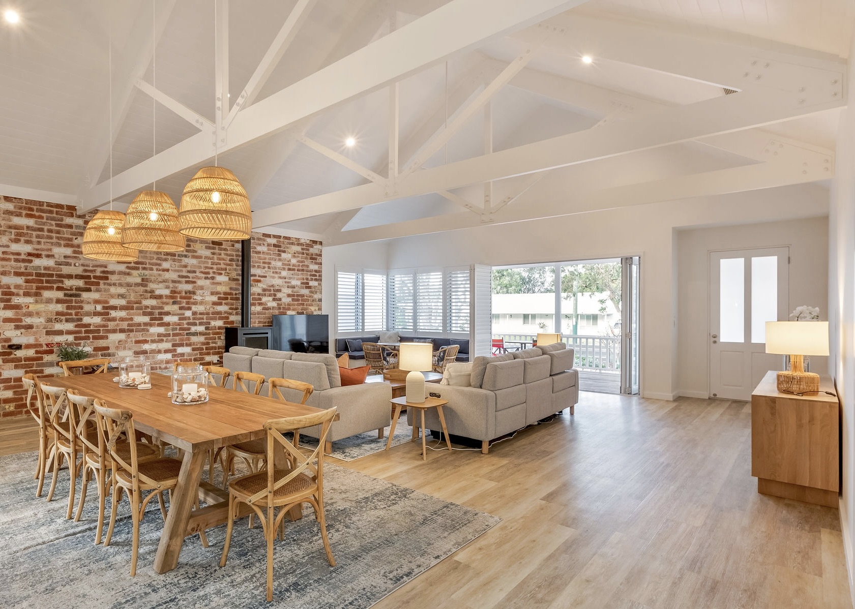 Open-plan living and dining with exposed trusses and feature brick wall