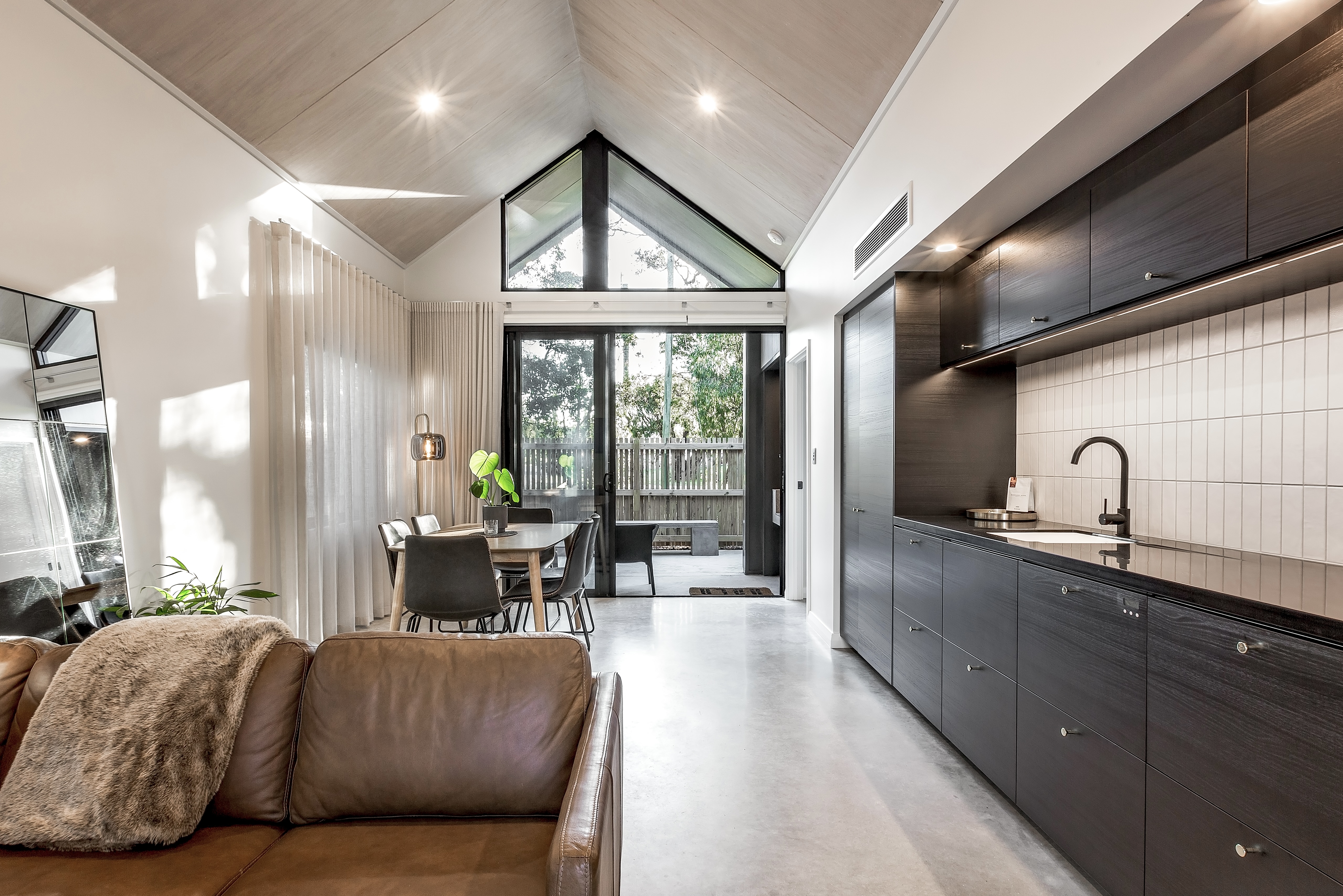 Double volume living area with whitewashed cathedral ceiling and dark kitchen joinery