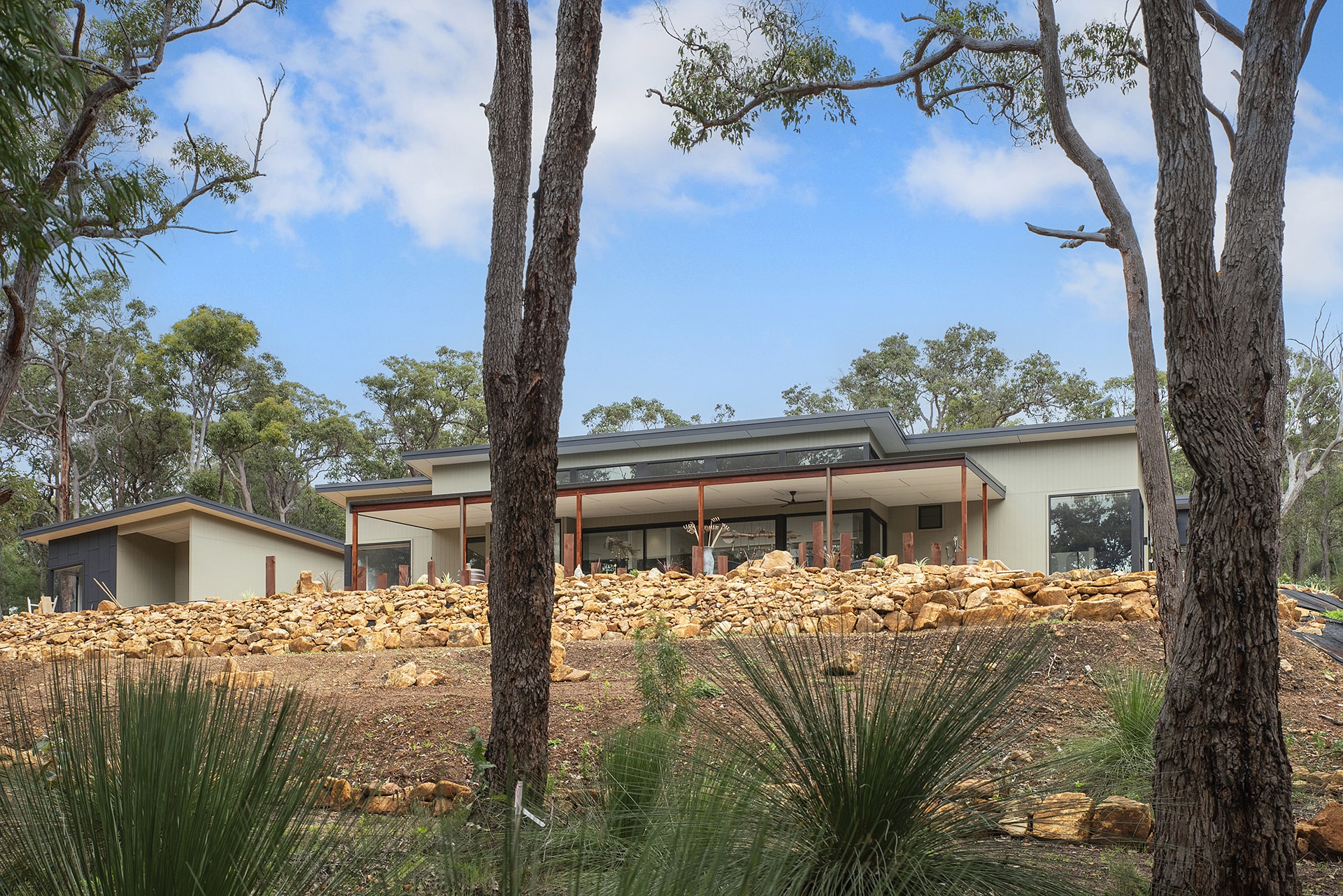 Modern architectural home nestled among native bushland with timber posts and rock landscaping in South West WA