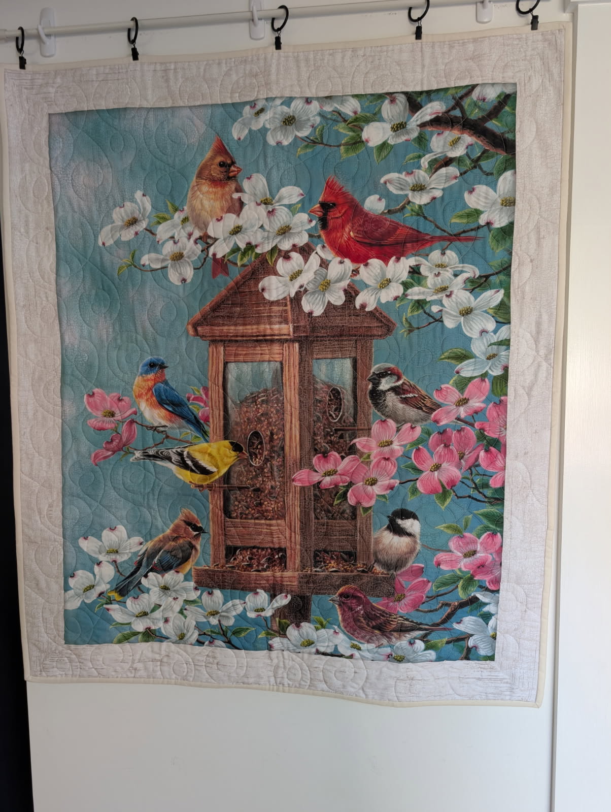 Wall hanging quilt panel of songbirds at a bird feeder surrounded by dogwood flowers