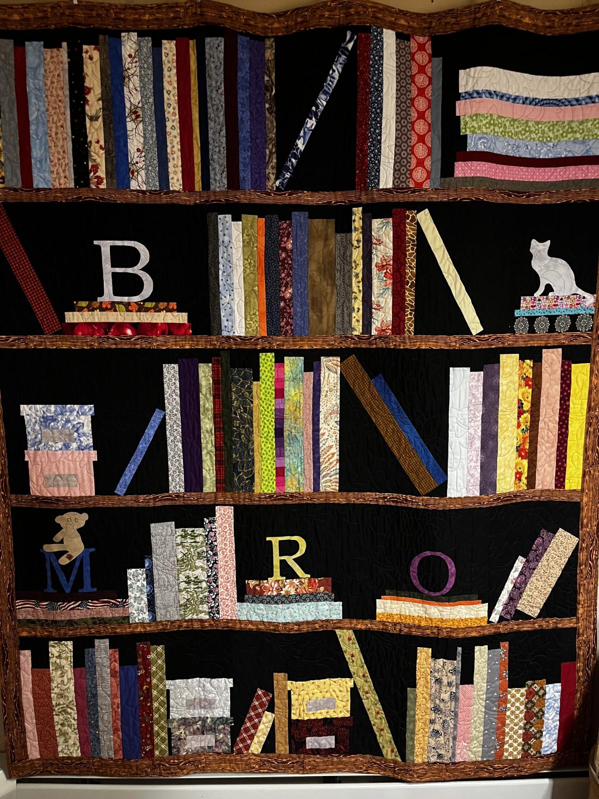Quilt designed to look like a bookshelf with fabric book spines and appliqued initials