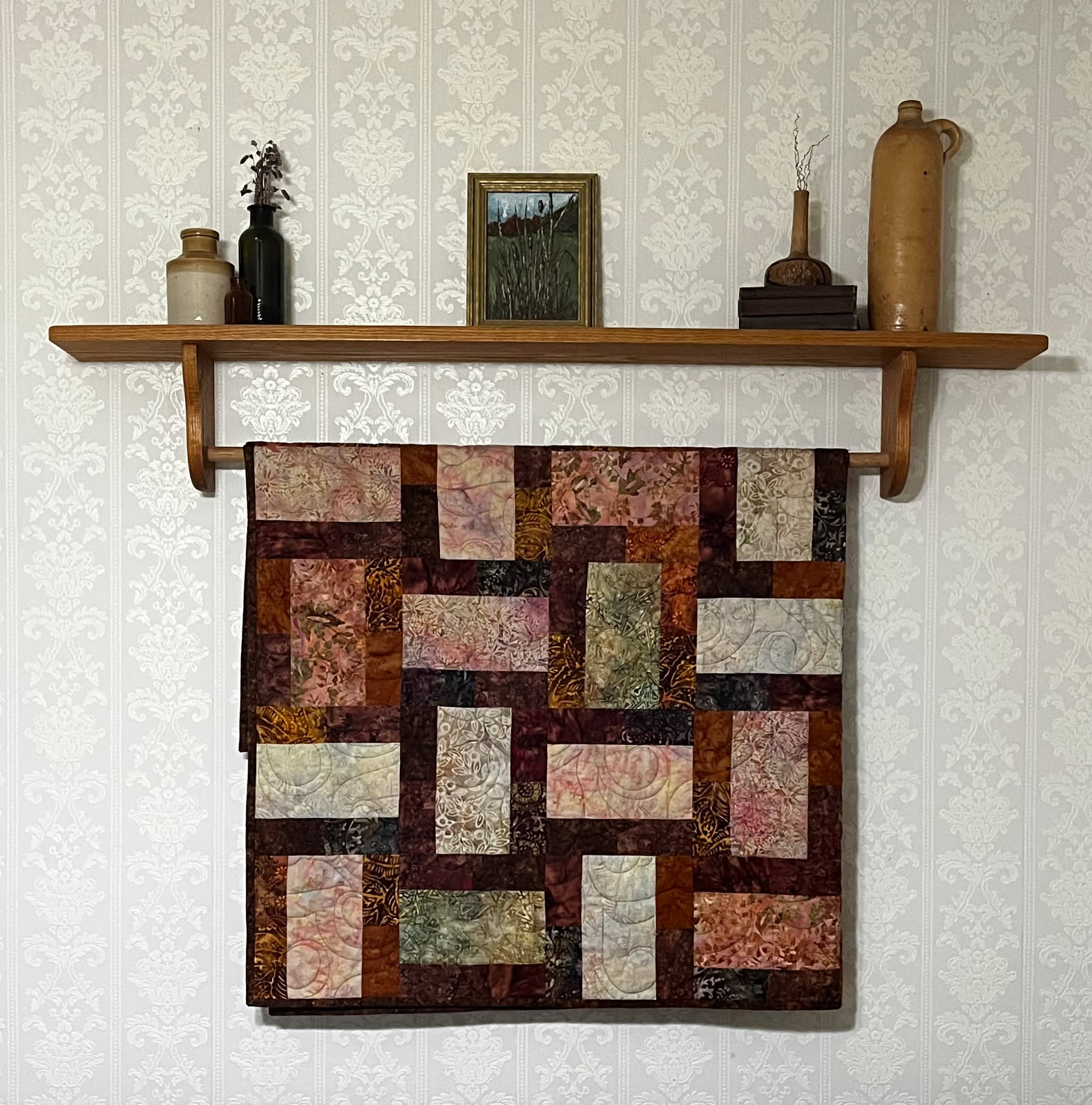 Batik quilt in brick pattern with plum, rust and sage tones draped on a wooden rack