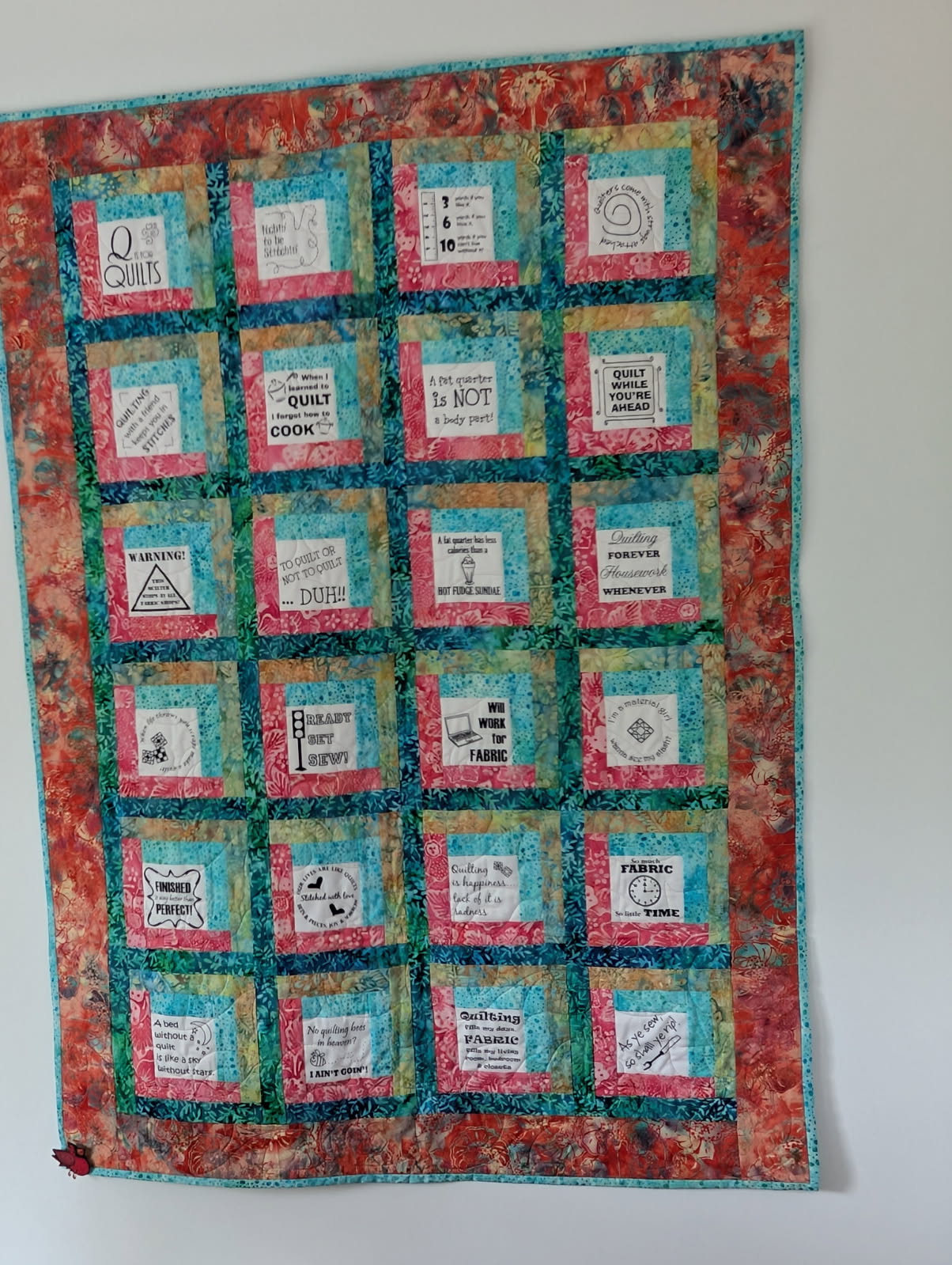Sampler quilt with embroidered quilting sayings in pink and teal batik fabrics