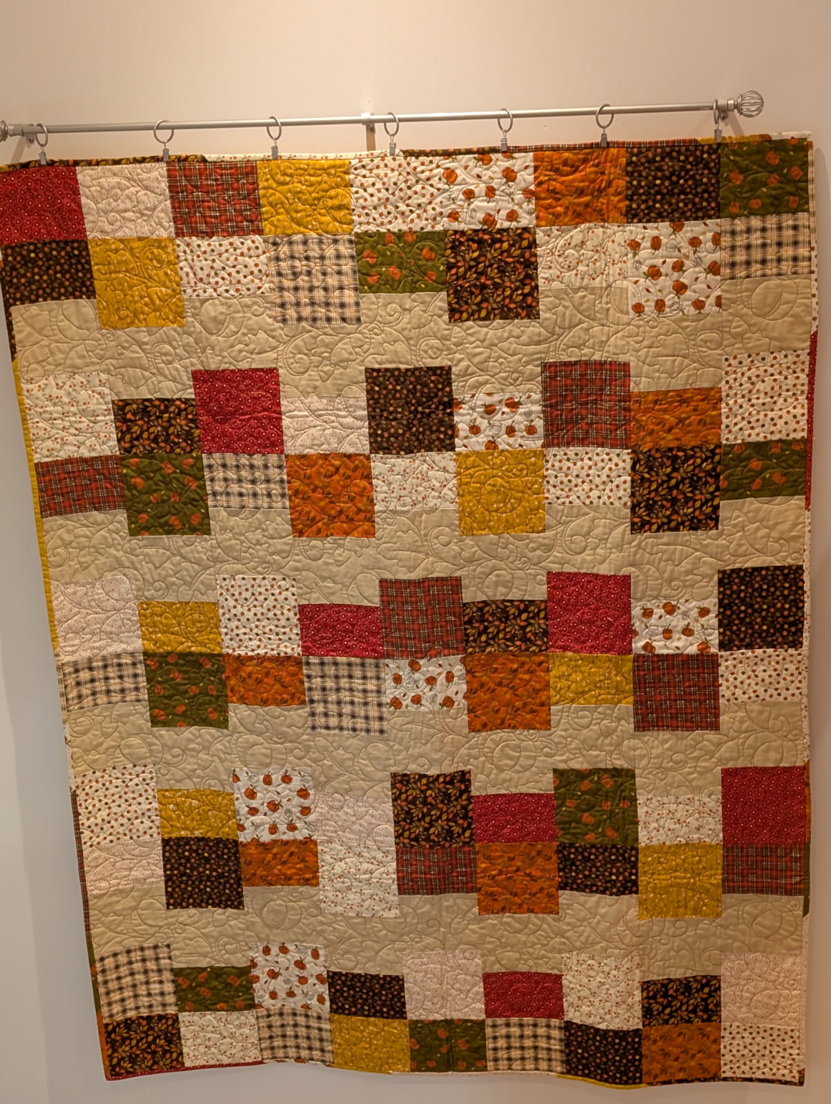 Patchwork quilt in autumn colors with pumpkin, plaid and dot fabrics hung on a wall