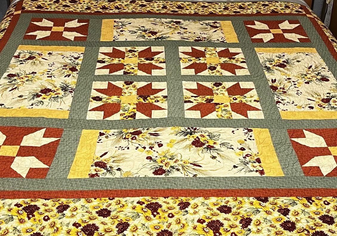 Sampler quilt with pieced star blocks and sunflower fabric panels in rust, gold and sage