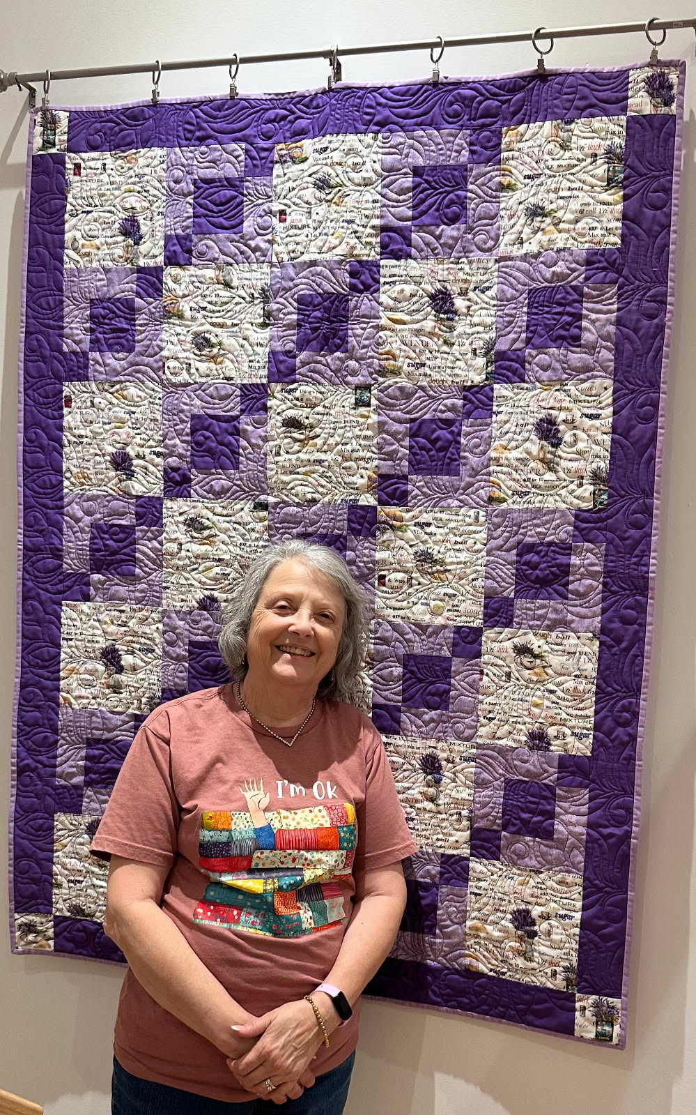 Purple and lavender quilt with recipe print fabric hung on a display rod