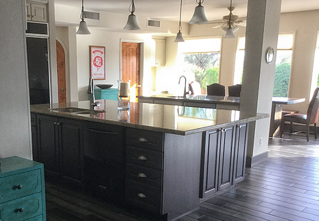 Expansive dark island with double sink, multiple pendant lights, and gray tile flooring