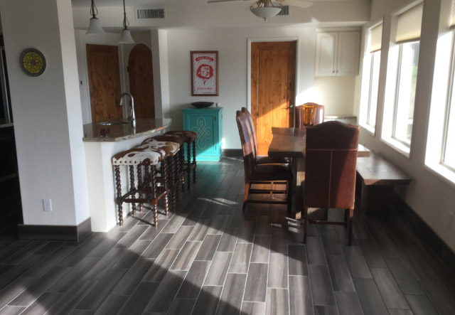Kitchen peninsula bar with seating, prep sink, and plank tile flooring leading to dining area