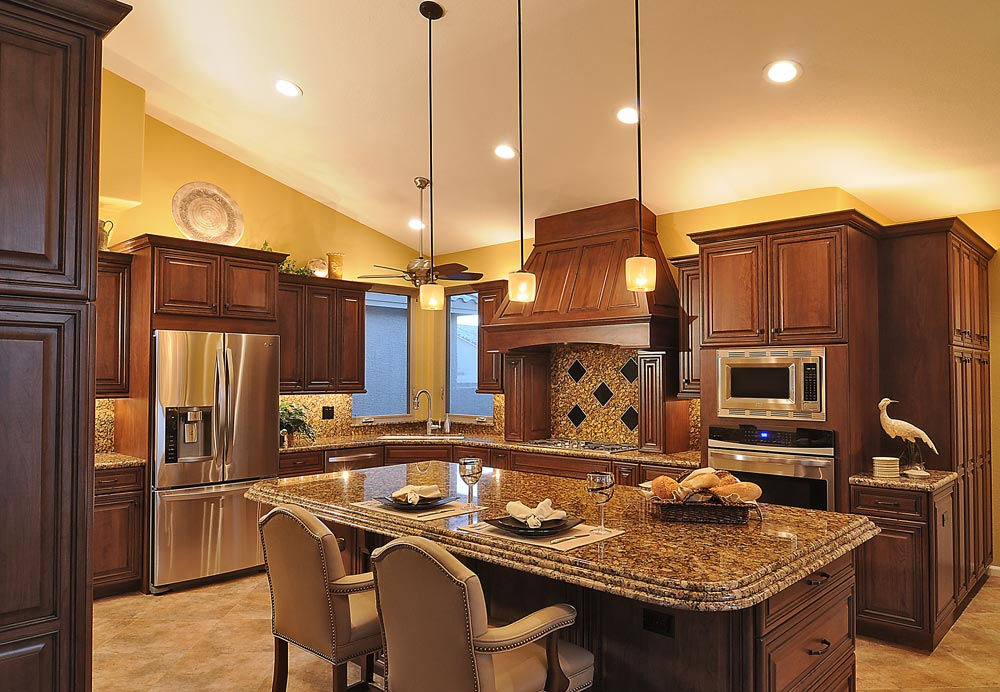 Architectural wood range hood with cooktop, wall oven, stainless appliances and granite island