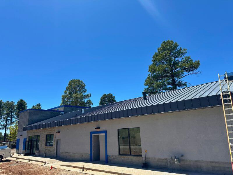Commercial standing seam metal roof installation in Northern Arizona with dark charcoal panels and pine tree backdrop