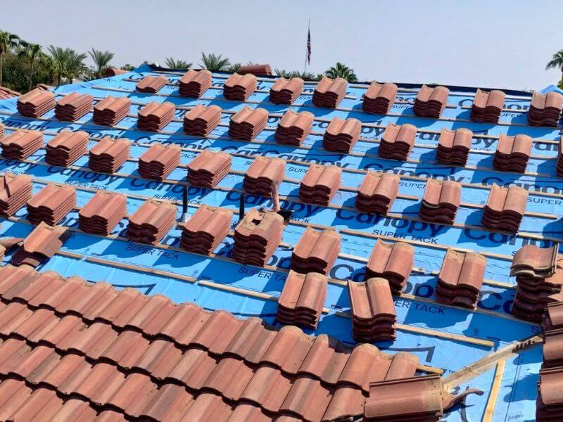 Concrete tiles stacked on blue underlayment during installation on Chandler Arizona apartment complex roof