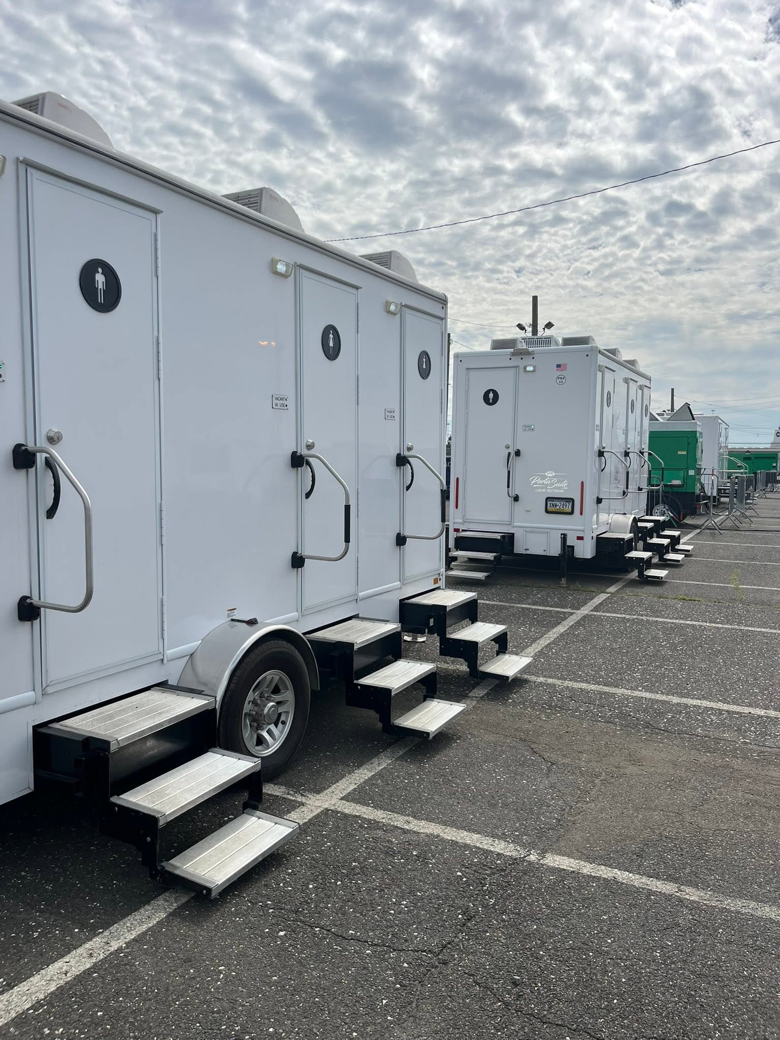 Line of white restroom trailers parked in a row on parking lot pavement with aluminum entry steps