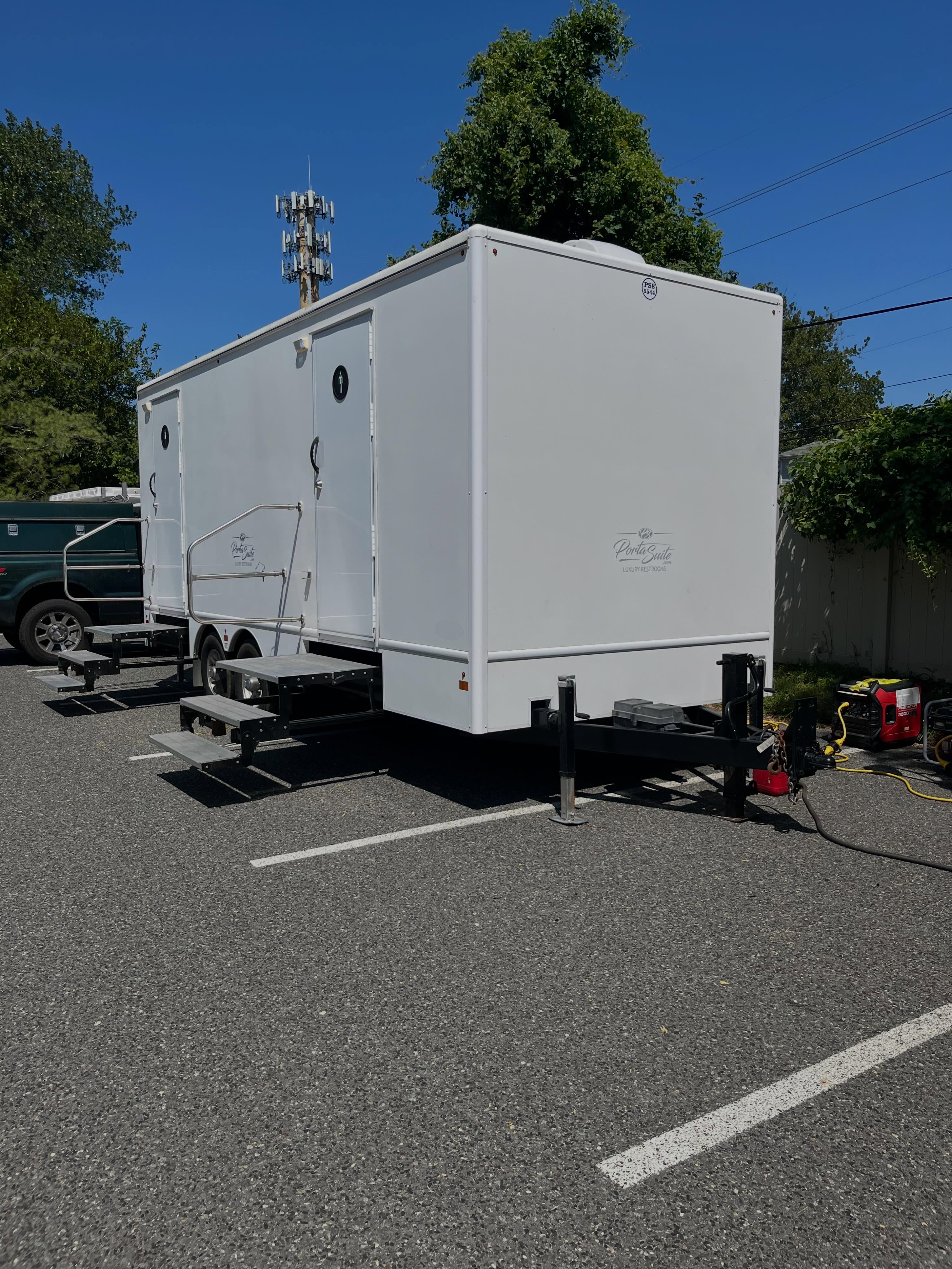 Clean white restroom trailer rental unit parked at an outdoor event on firm level paved ground