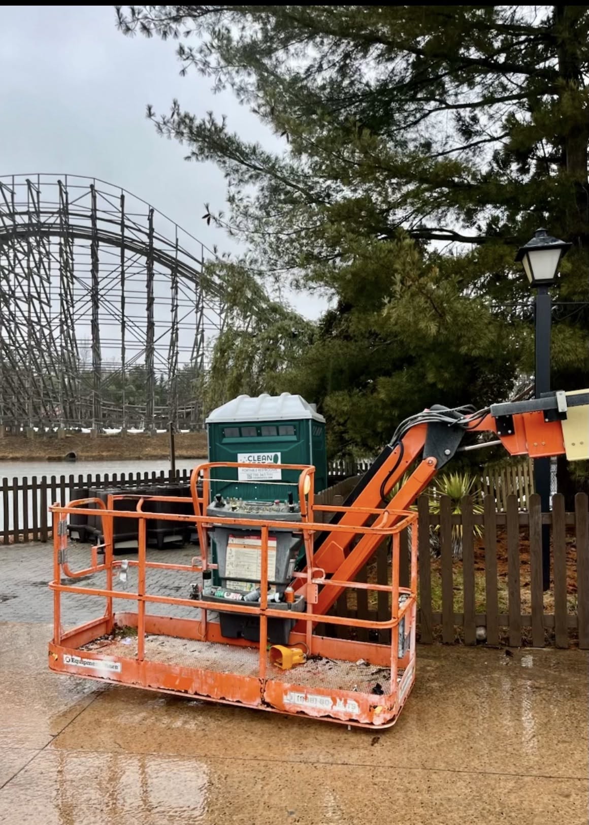 Green portable restroom placed near a fence and construction lift at an outdoor project location on Long Island
