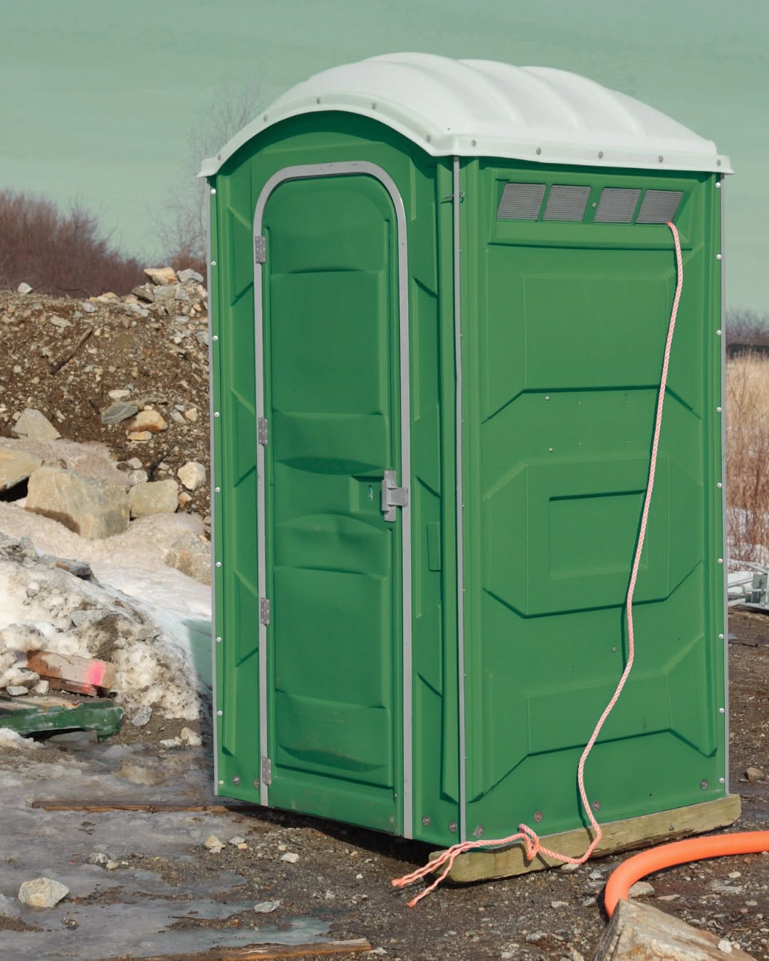 Standard portable toilet positioned on firm level ground at an active residential construction job site on Long Island, NY