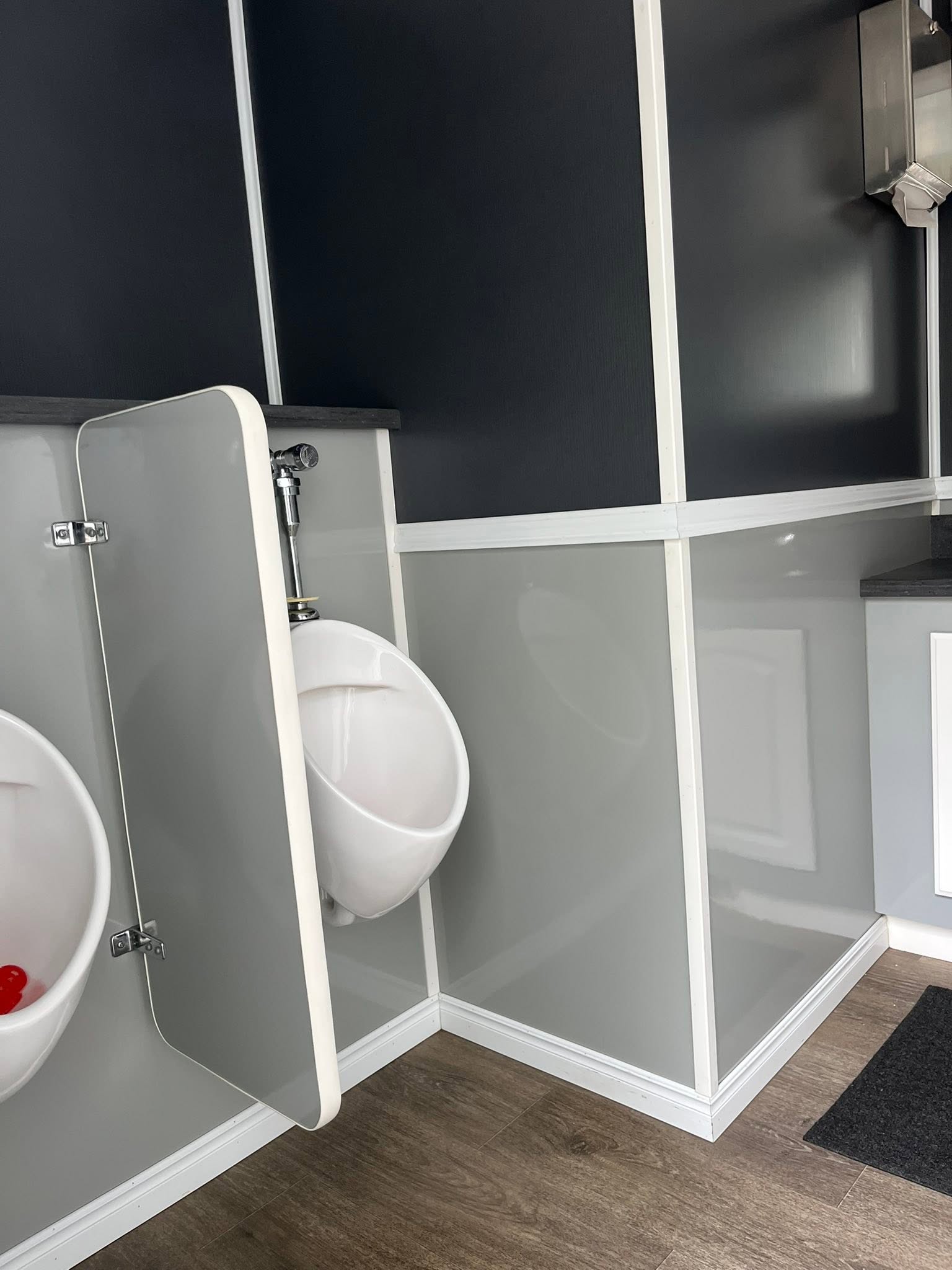 Immaculate interior of a luxury restroom trailer with modern urinals, wall paneling, and wood-style flooring