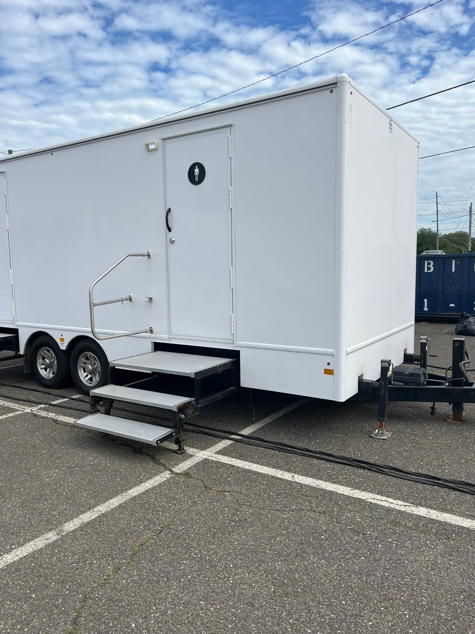 White multi-stall restroom trailer staged on parking lot asphalt with heavy-duty stairs and handrails