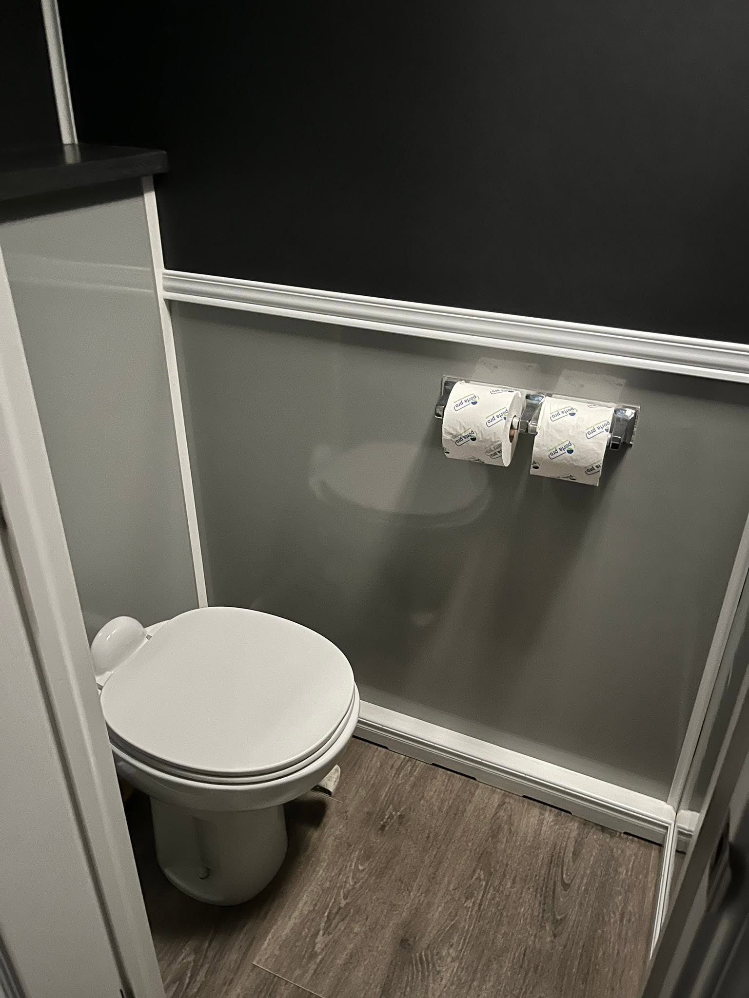 Clean restroom trailer stall interior with flush toilet, wainscoting, and wood-grain flooring