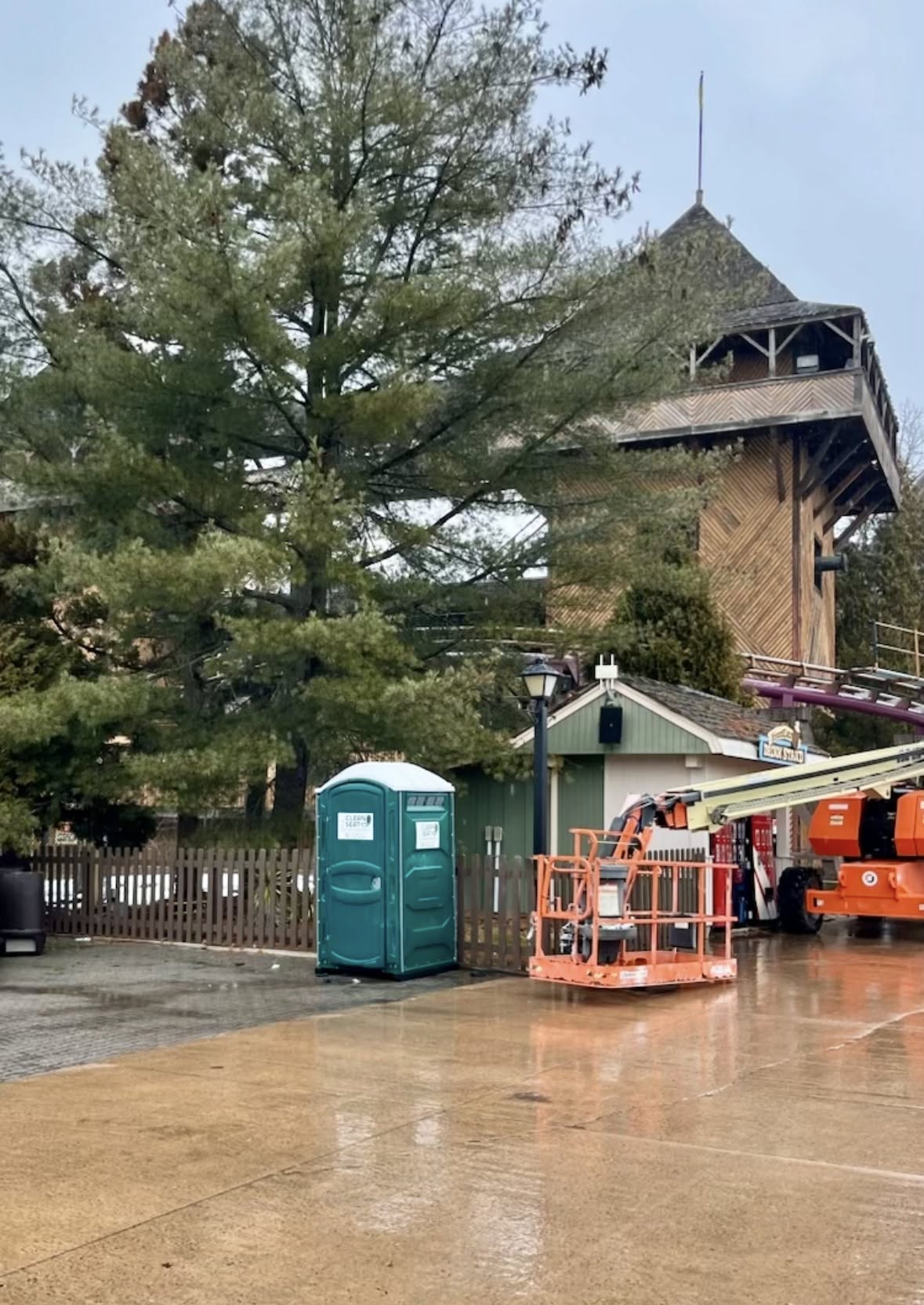 Green portable toilet staged on pavement beside heavy lift equipment at a commercial job site on Long Island
