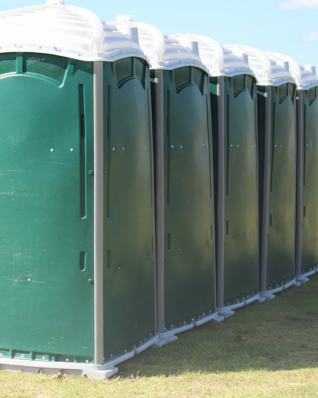 Row of clean green portable restrooms lined up neatly on grass for a Long Island event setup
