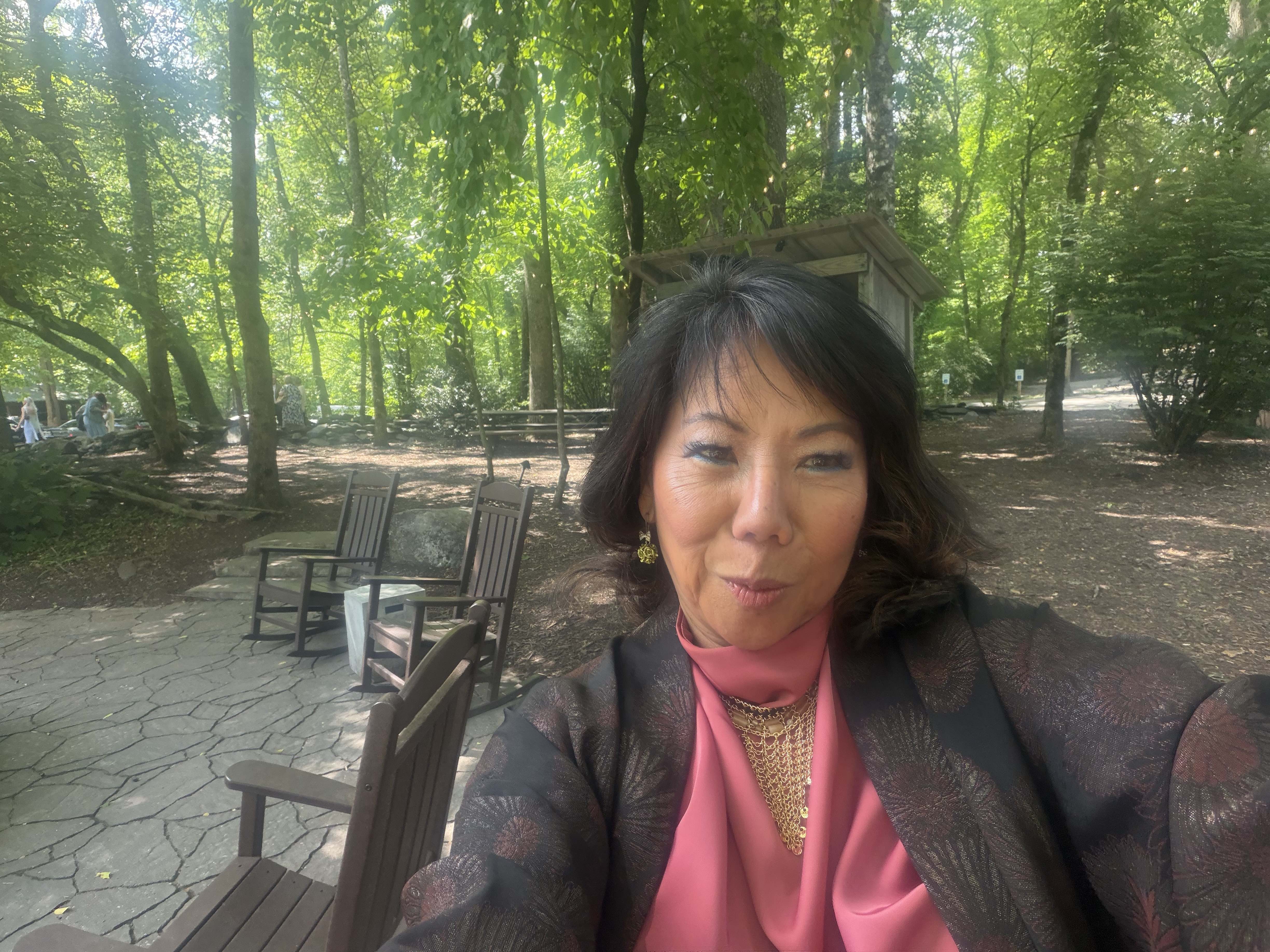 Rosanna Iosso, Mindlayers Certified Hypnotherapist, seated peacefully in a sunlit garden with wooden benches and lush green trees
