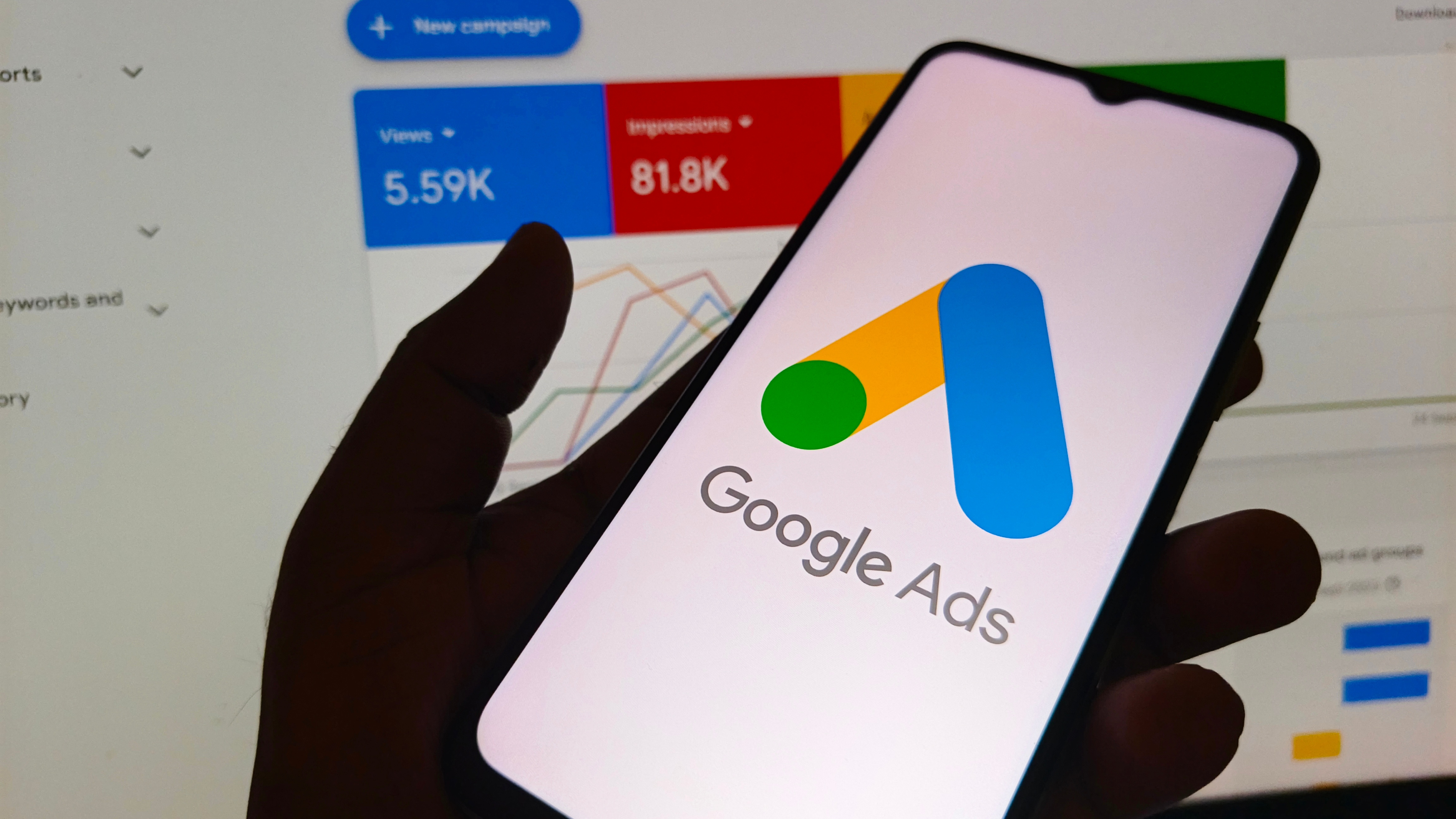 Google Ads dashboard on phone with analytics in background