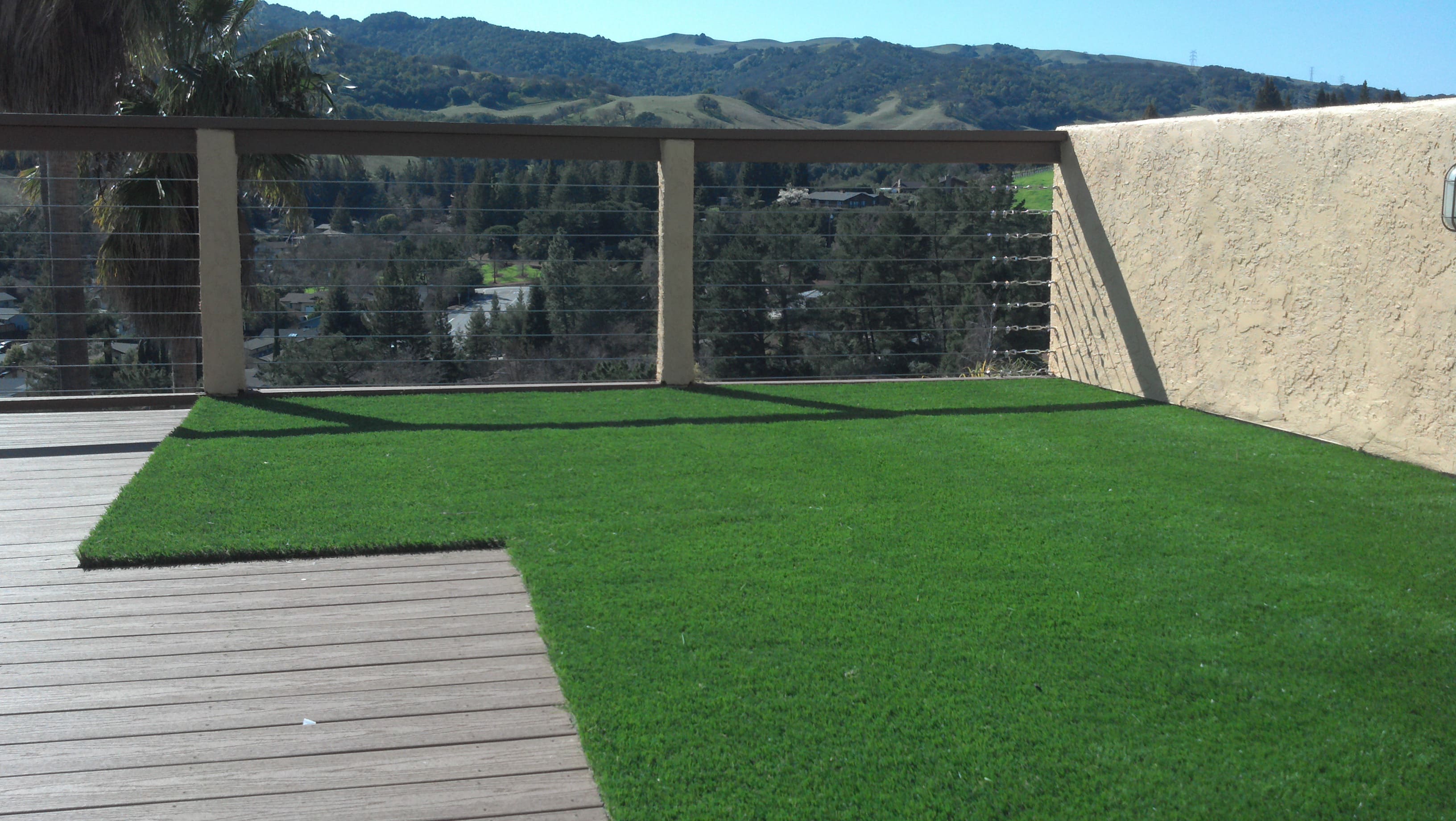 Spacious backyard paver patio with built-in seating, deck area, and lush synthetic turf lawn - Paradise Building Materials project in Brentwood, CA