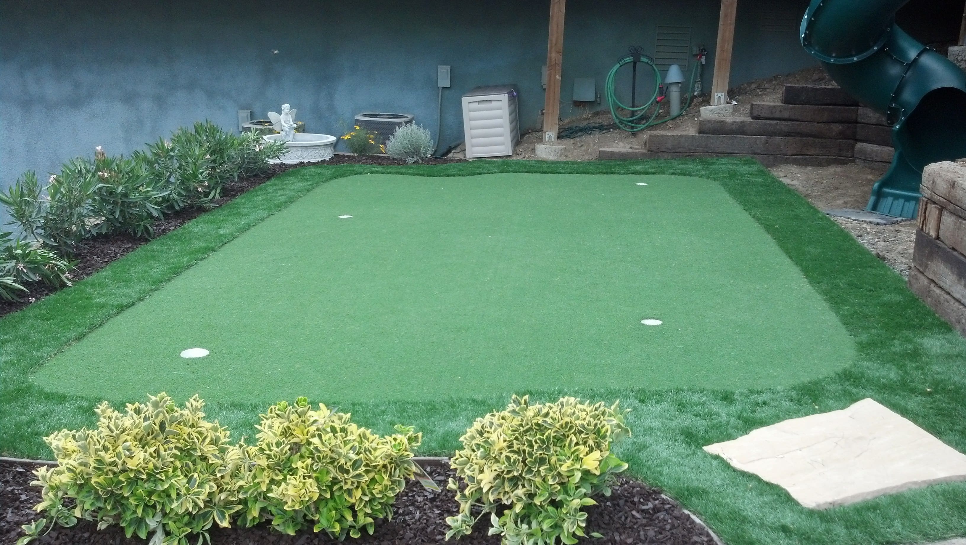 Synthetic turf putting green in a family backyard with flagstone stepping stones - Paradise Building Materials project