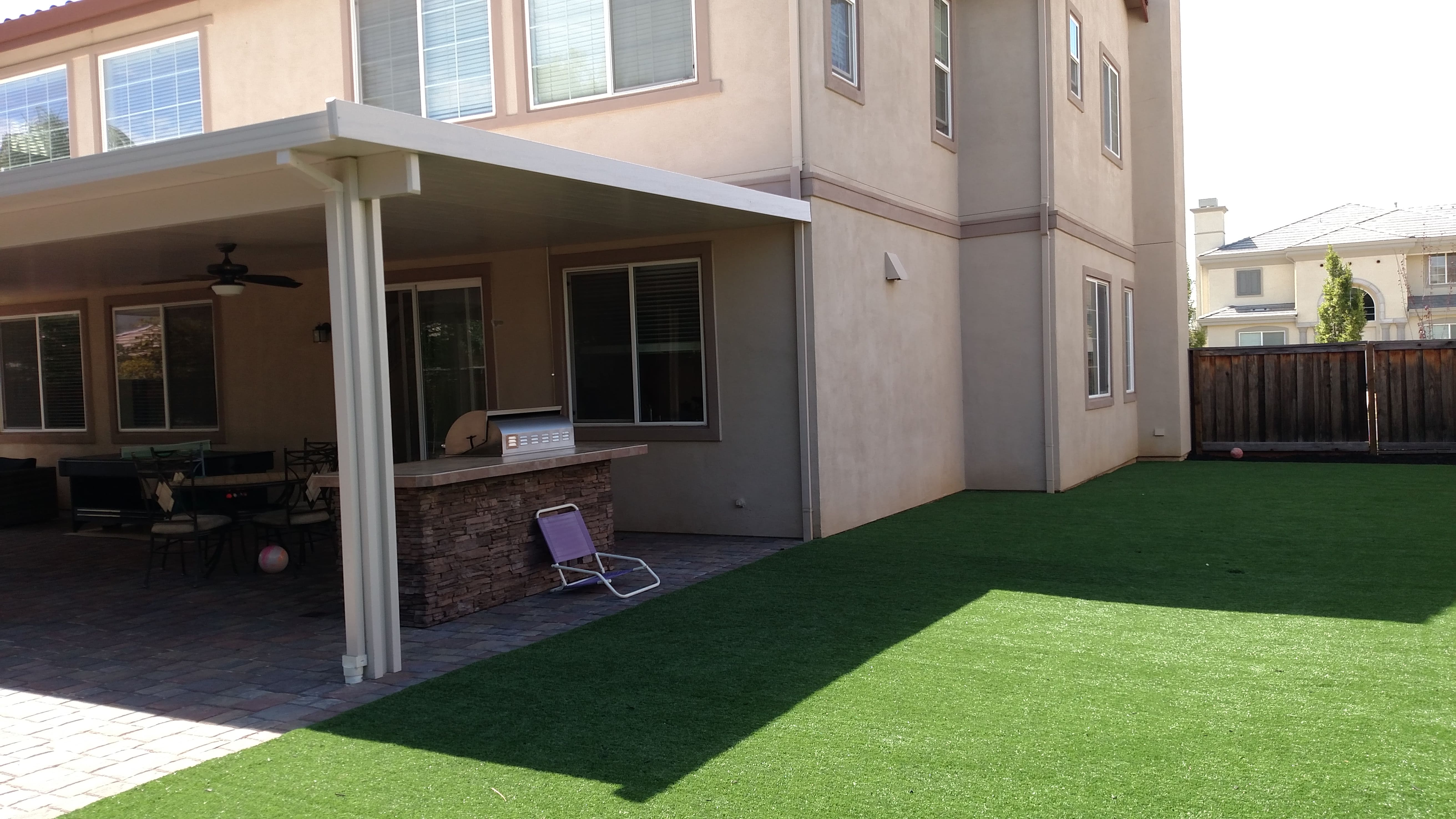 Backyard transformation featuring synthetic turf lawn, paver patio, and outdoor kitchen - all materials from Paradise Building Materials