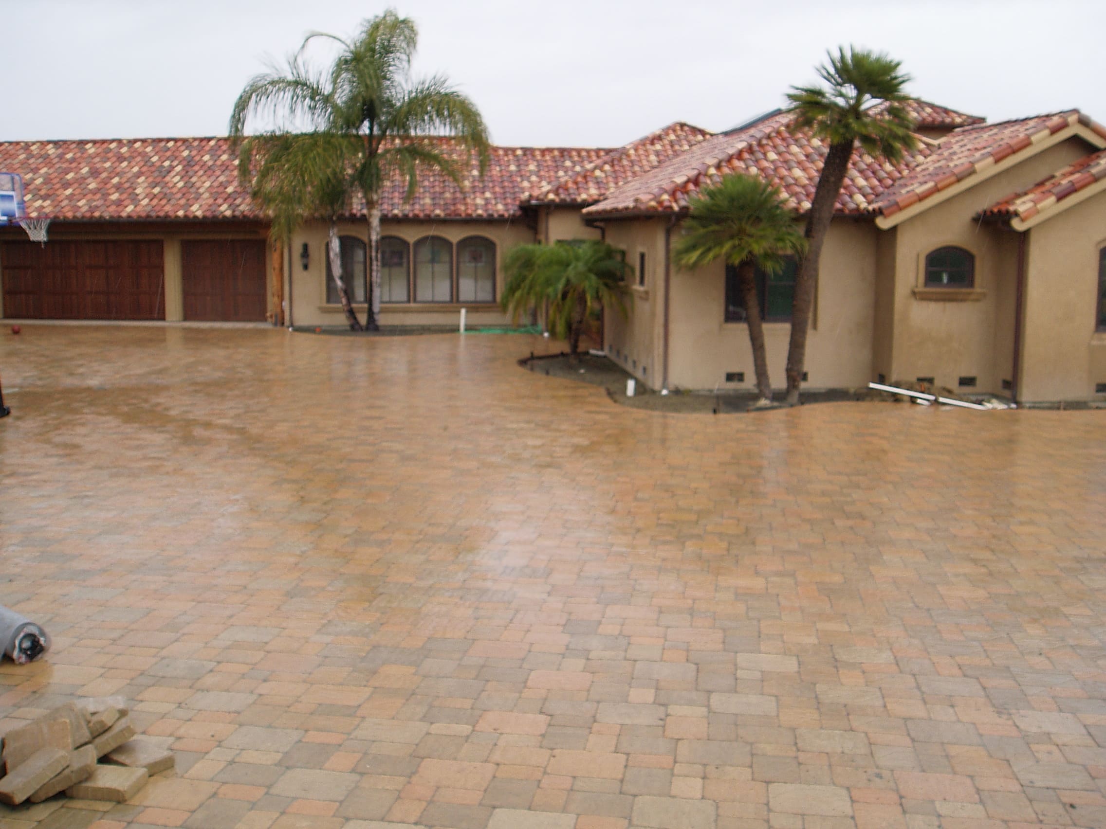 Large interlocking paver driveway at Mediterranean home with clay tile roof and palm trees - Paradise Building Materials project
