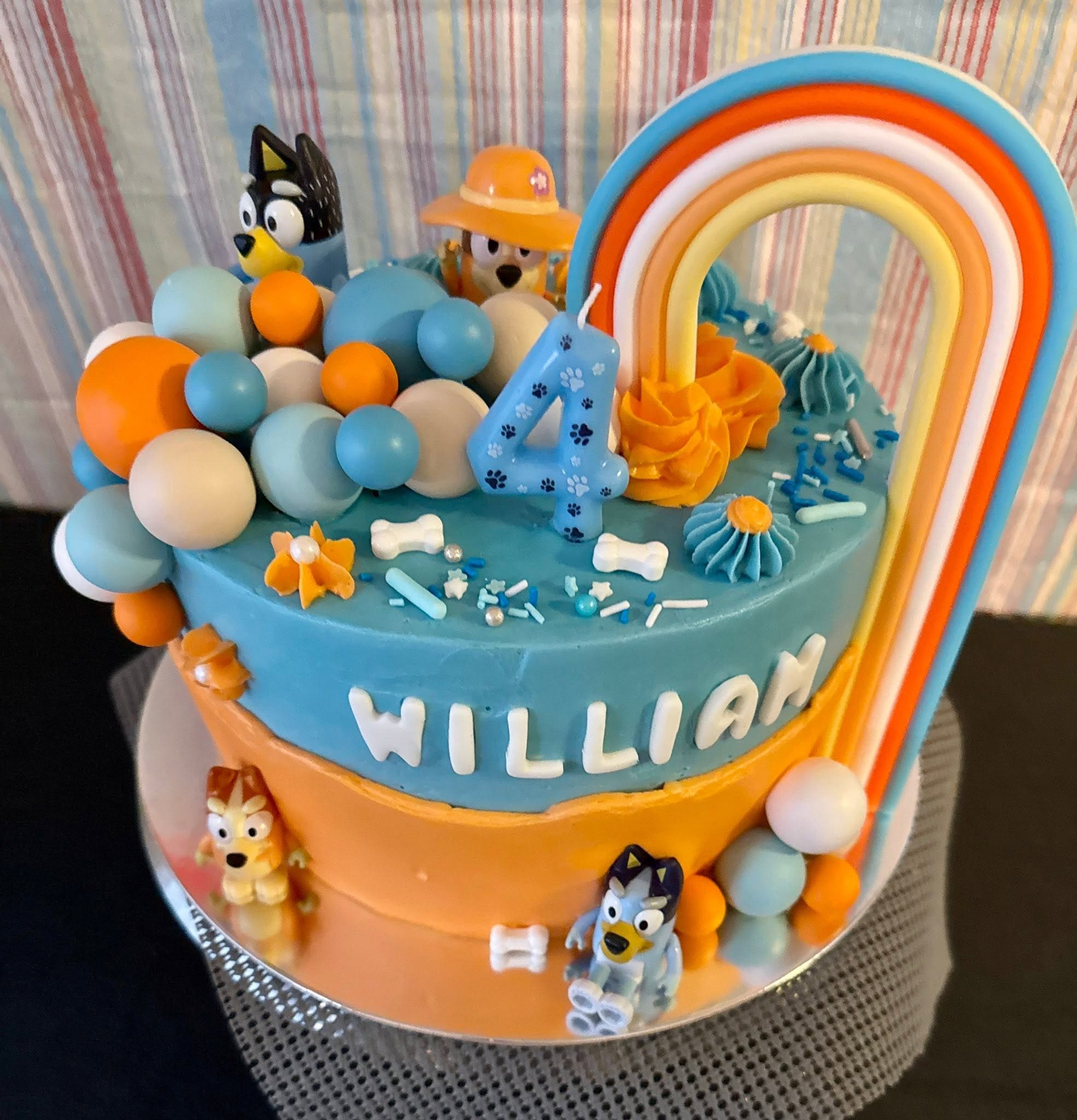 Custom Bluey themed birthday cake with rainbow arch characters and name lettering by Sweet Tooth Creations Anchorage bakery