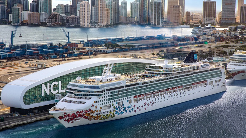 Daytime view of a Norwegian cruise ship docked at the modern PortMiami terminal with the downtown Miami skyline in the background