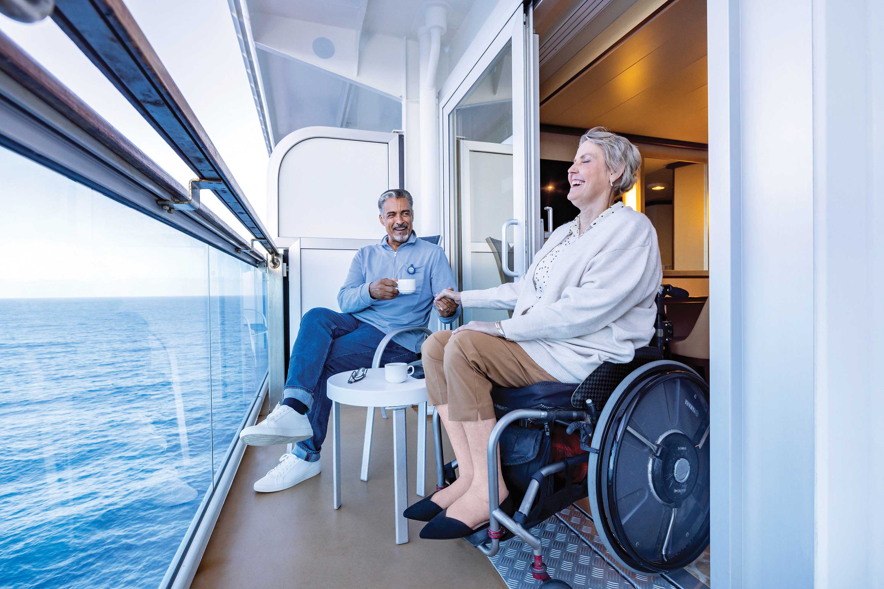 Smiling couple enjoying ocean views and coffee on an accessible cruise ship private balcony with wheelchair accommodation