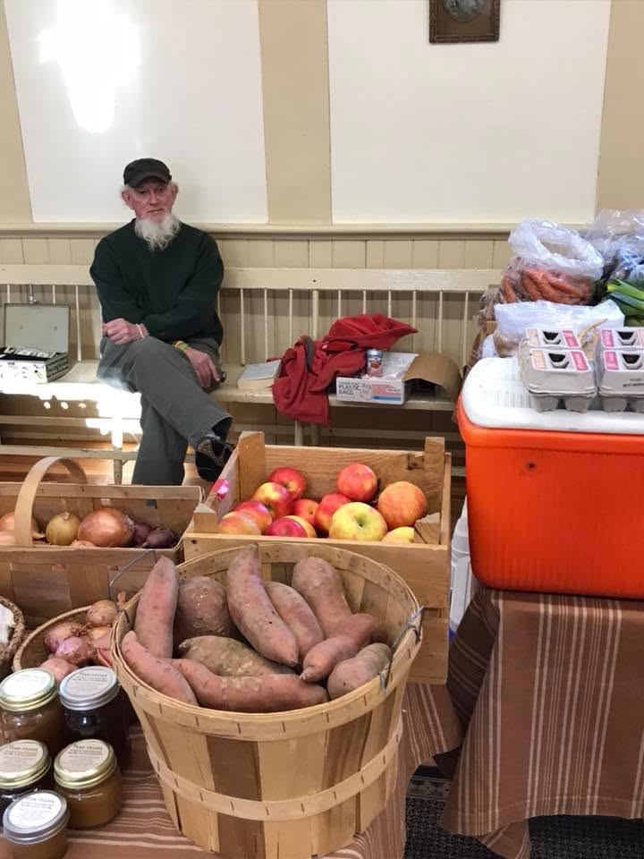 Farmers market inside the Grange hall featuring local produce including apples, sweet potatoes, and preserves
