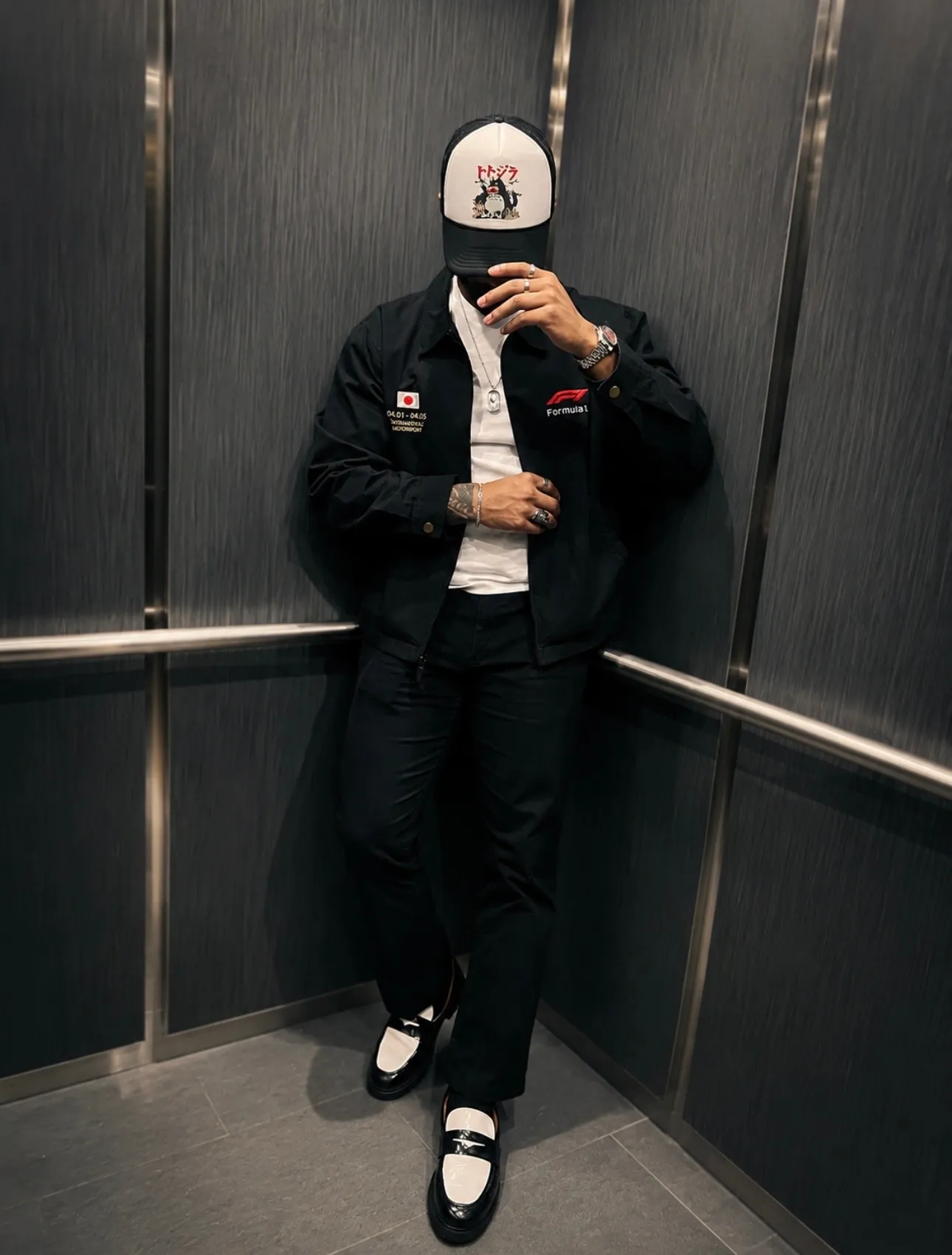Jai'koa Parham in an elevator wearing a black F1 jacket, white tee, and trucker cap, commercial streetwear campaign