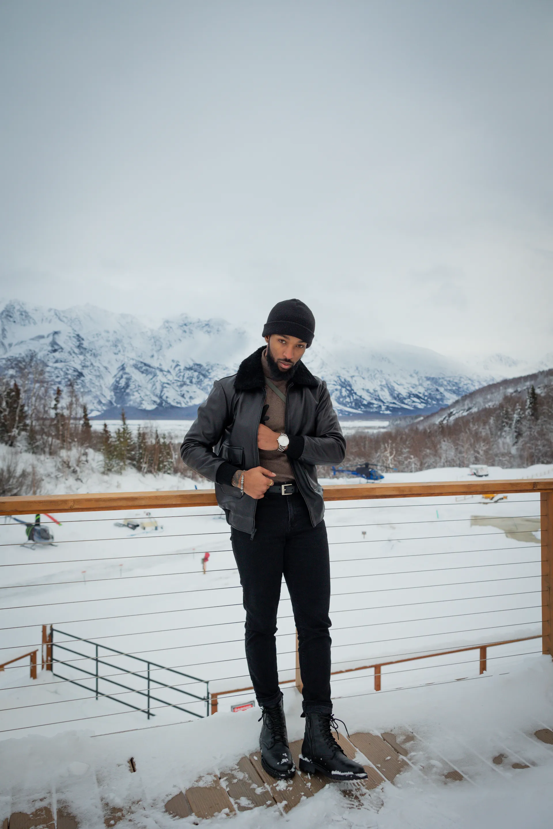 Jai'koa Parham in a black leather shearling jacket with snowy Alaskan mountains in the background, outdoor travel campaign