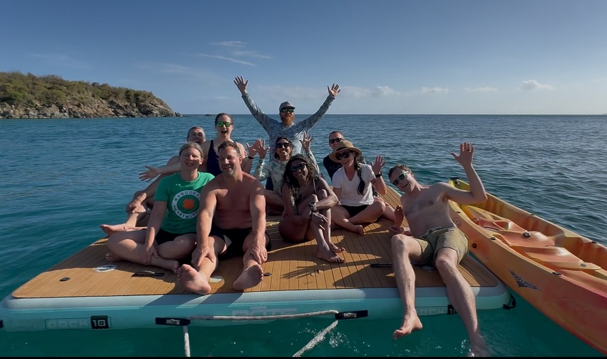 Guests relaxing on a floating platform behind Touch the Sky catamaran