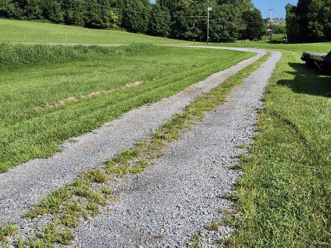 Gravel driveway with washboarding, ruts, and grass encroachment before repair work