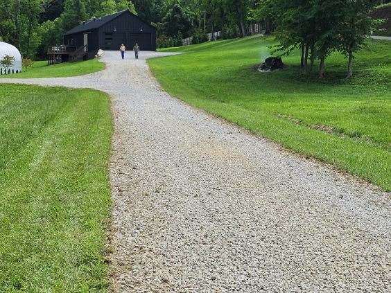 Long restored gravel driveway through pasture land with black barn and house in background