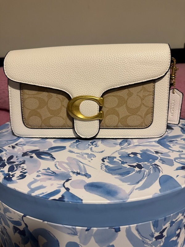 White cream Coach leather shoulder bag with large gold C buckle hardware beige signature monogram front panel flap closure displayed on blue white floral patterned round box