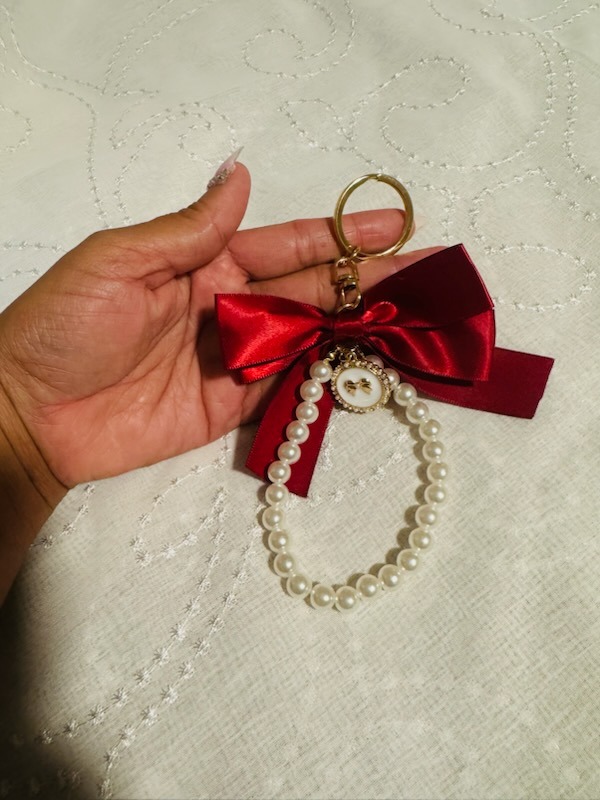 Luxury designer keychain featuring a rich crimson red satin bow, gold keyring, and pearl bead wristlet strap with gold bow charm