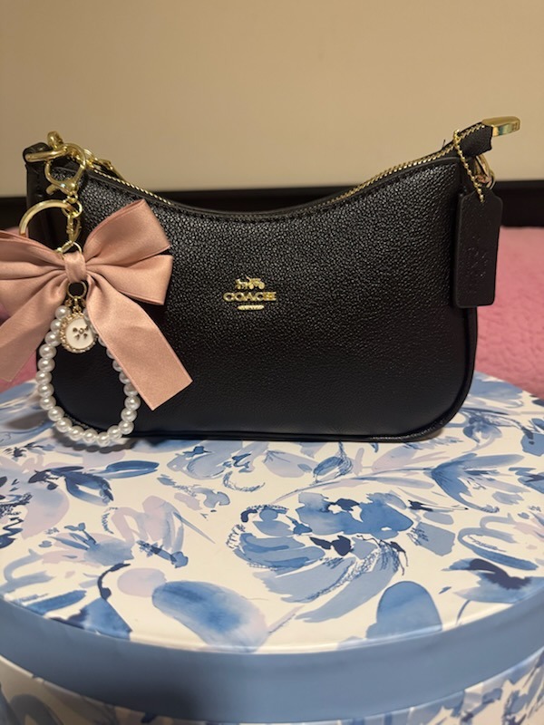 Black Coach leather textured shoulder bag with pink satin bow charm pearl beaded keychain gold zipper hardware black leather COACH tag on floral patterned display box
